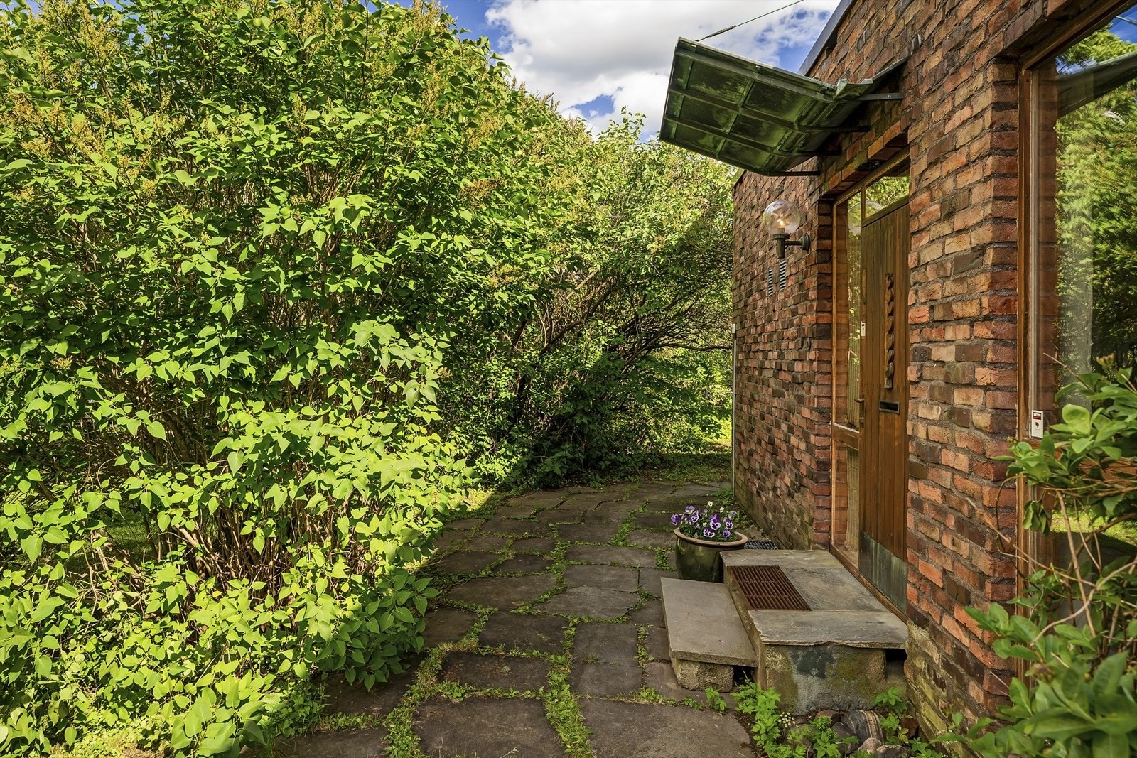 Velkommen hjem! Innbydende inngangsparti med belysning ved døren. Syriner og villvind smyger seg dekorativt rundt inngangspartiet. Galleribilde