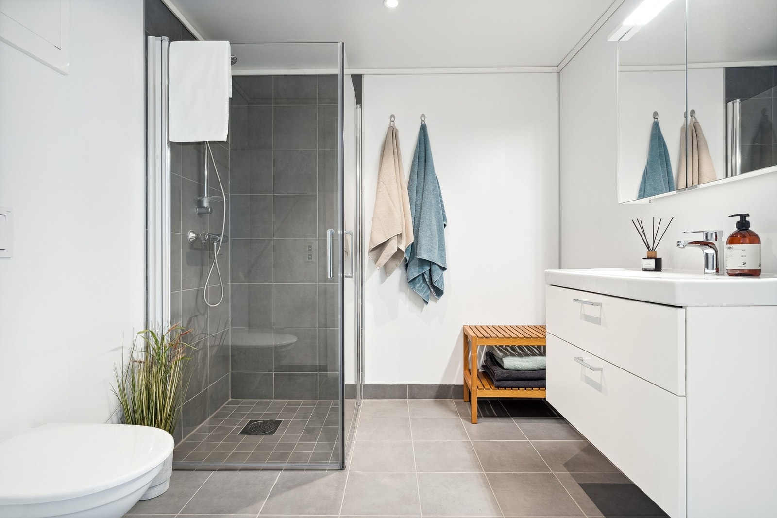 Bad utstyrt med innfellbare dusjdører, mekanisk avtrekk, servant, servantskap, rørfordelingsskap, stoppekran, vannmåler og veggmontert wc. Galleribilde