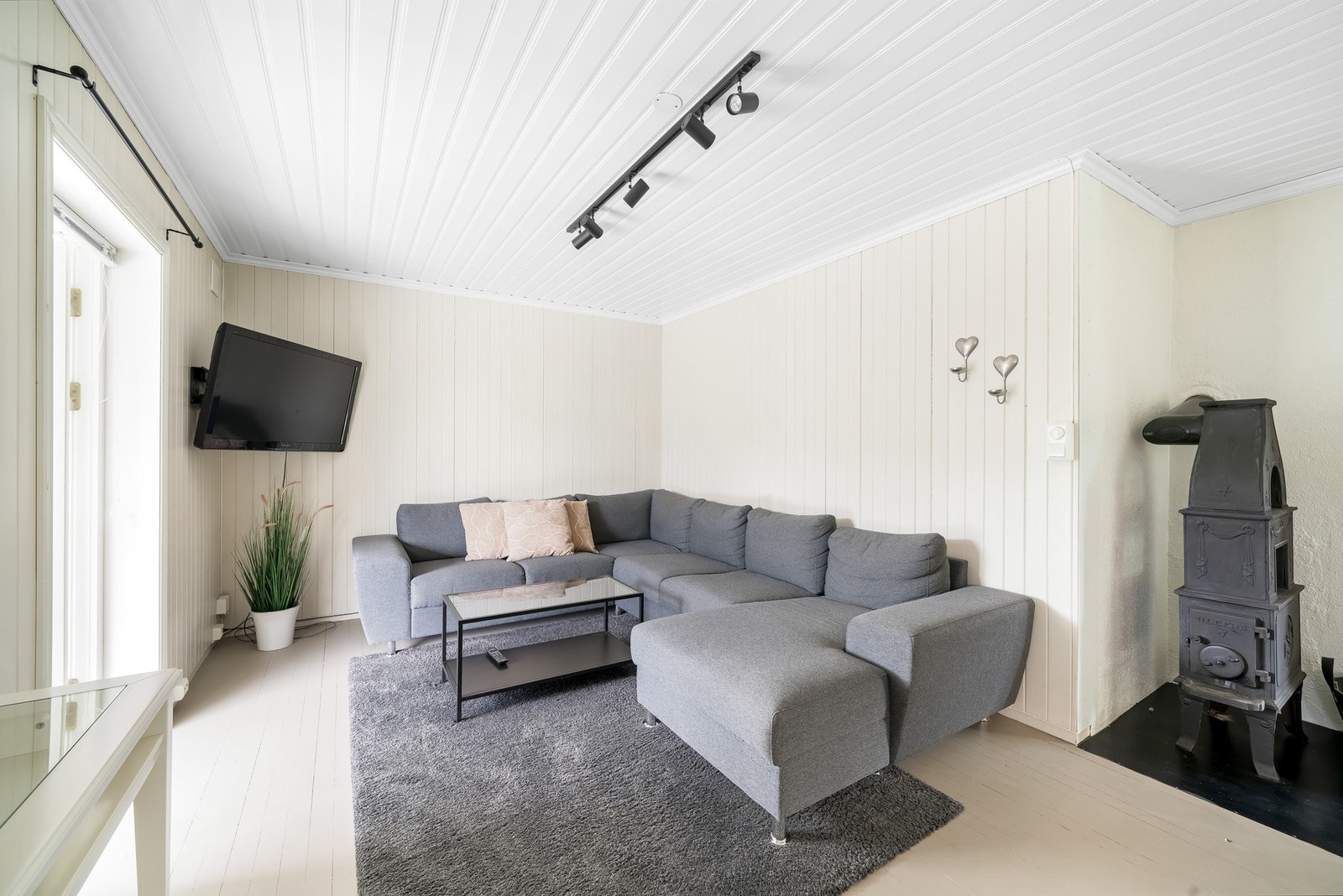Stue i 1. etasje har malt trepanel på veggene og i himling, samt malt heltre gulvbord. Ulefos etasjeovn. Fra stuen er det utgang til verandaen. Galleribilde