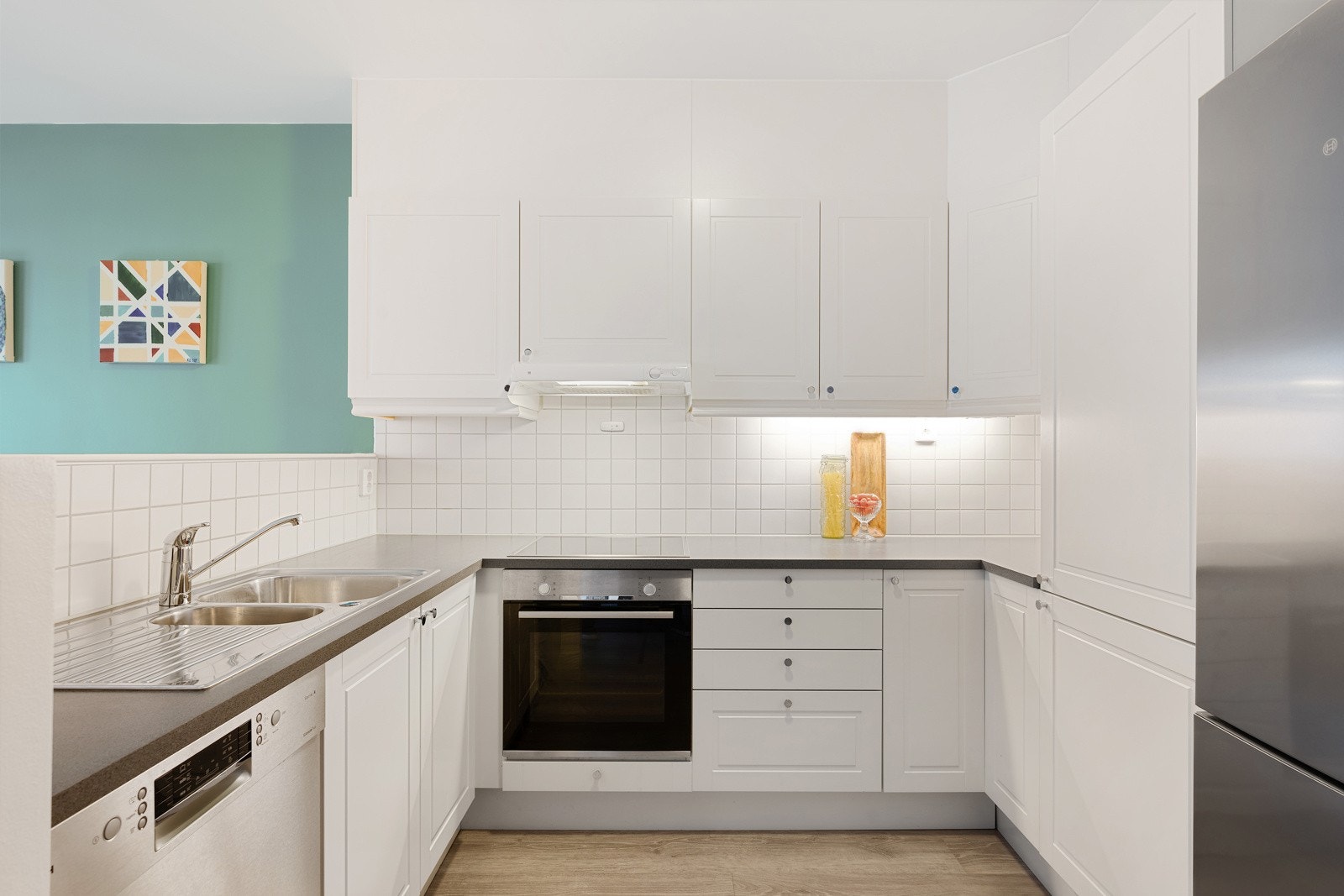 Innredningen er oppforet og har hvite, profilerte fronter, hvite fliser over benk, lys under overskap og laminert benkeplate med oppvaskkum Galleribilde