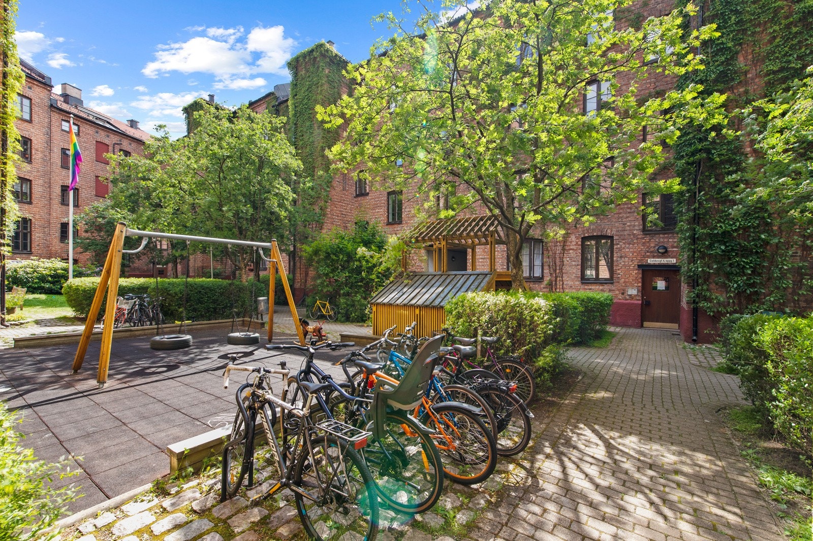 Lukket og pent gårdsrom med sittegrupper, beplantning, sandkasse for de minste og sykkelskur. Galleribilde