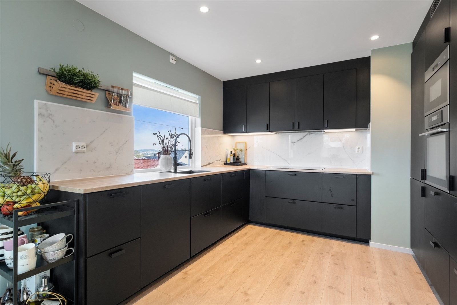 Kjøkkeninnredning i laminat med slette fronter. Det er ventilator over integrert koketopp, integrert stekeovn, mikrobølgeovn, oppvaskmaskin, kjøl- og fryseskap. Galleribilde