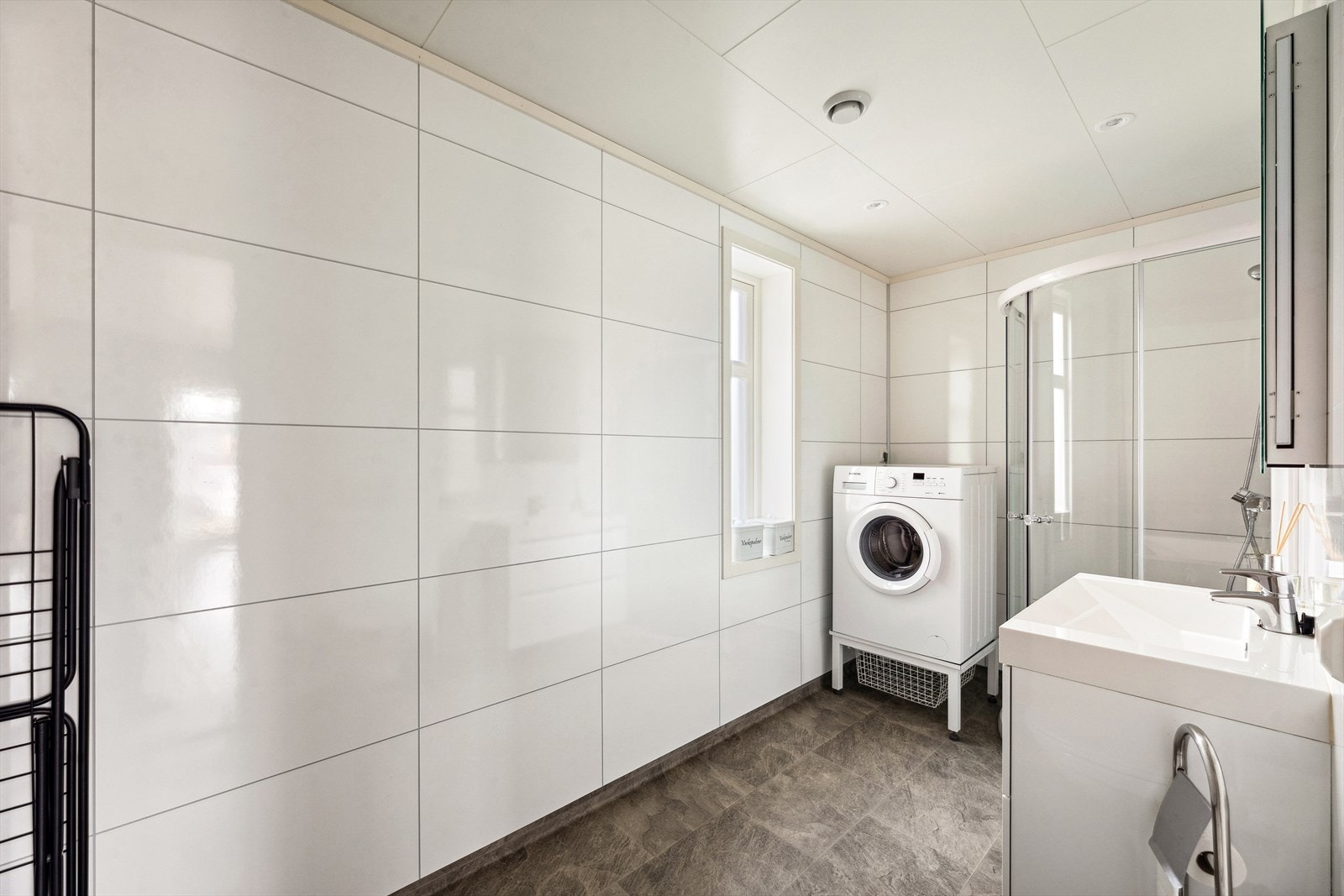 Badet inneholder vegghengt toalett, dusjhjørne, heldekkende servant med ett greps blandebatteri på skuffeinnredning, speil med lys, høyskap og opplegg for vaskemaskin. Galleribilde