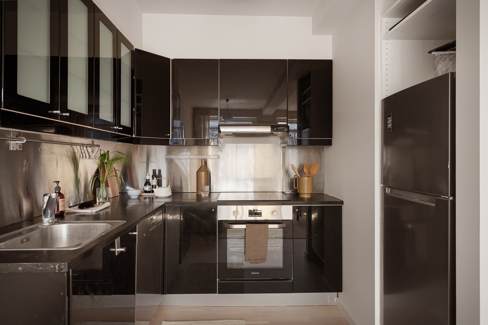 Pen og tidløs kjøkkeninnredning fra 2005 med svarte høyglans fronter, benkeplate av laminat og backsplash belagt med stålplate. Galleribilde