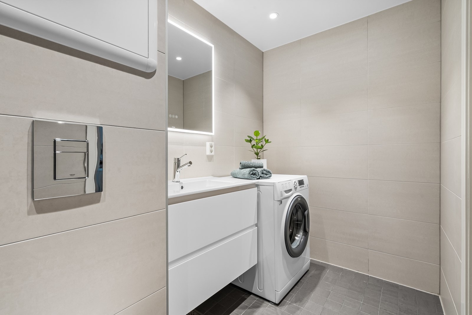 Servant i helstøpt plate med oppbevaring i skuffer, vegghengt speil med innebygget lys. Badet har i tillegg downlights i tak og opplegg for vaskemaskin. Galleribilde