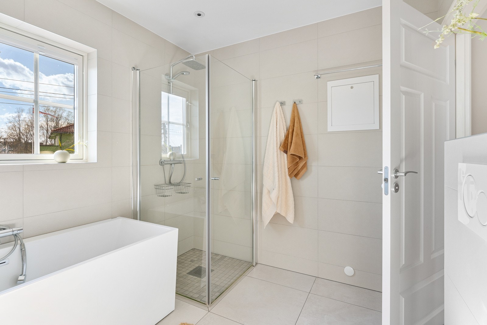 Baderommet inneholder vegghengt toalett, badekar, dusj med innfellbare glassdører og servant med underskap Galleribilde