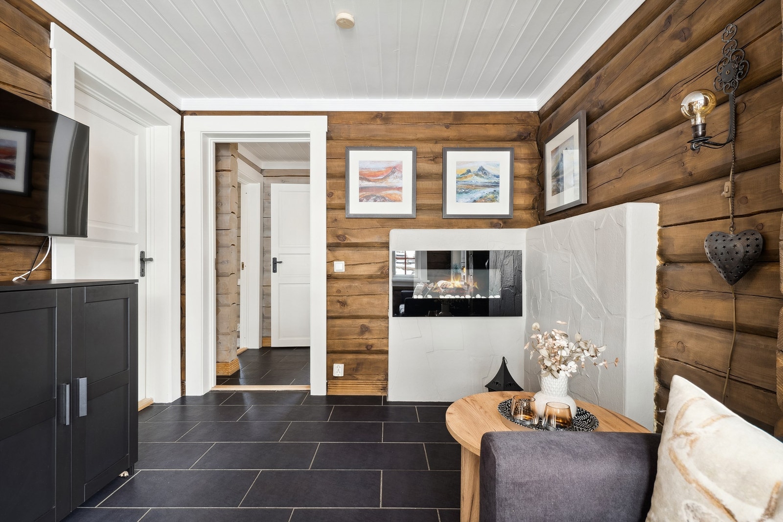 Romslig stue med mørke fliser på gulvet, sjarmerende tømmervegger og elektrisk peis. Galleribilde