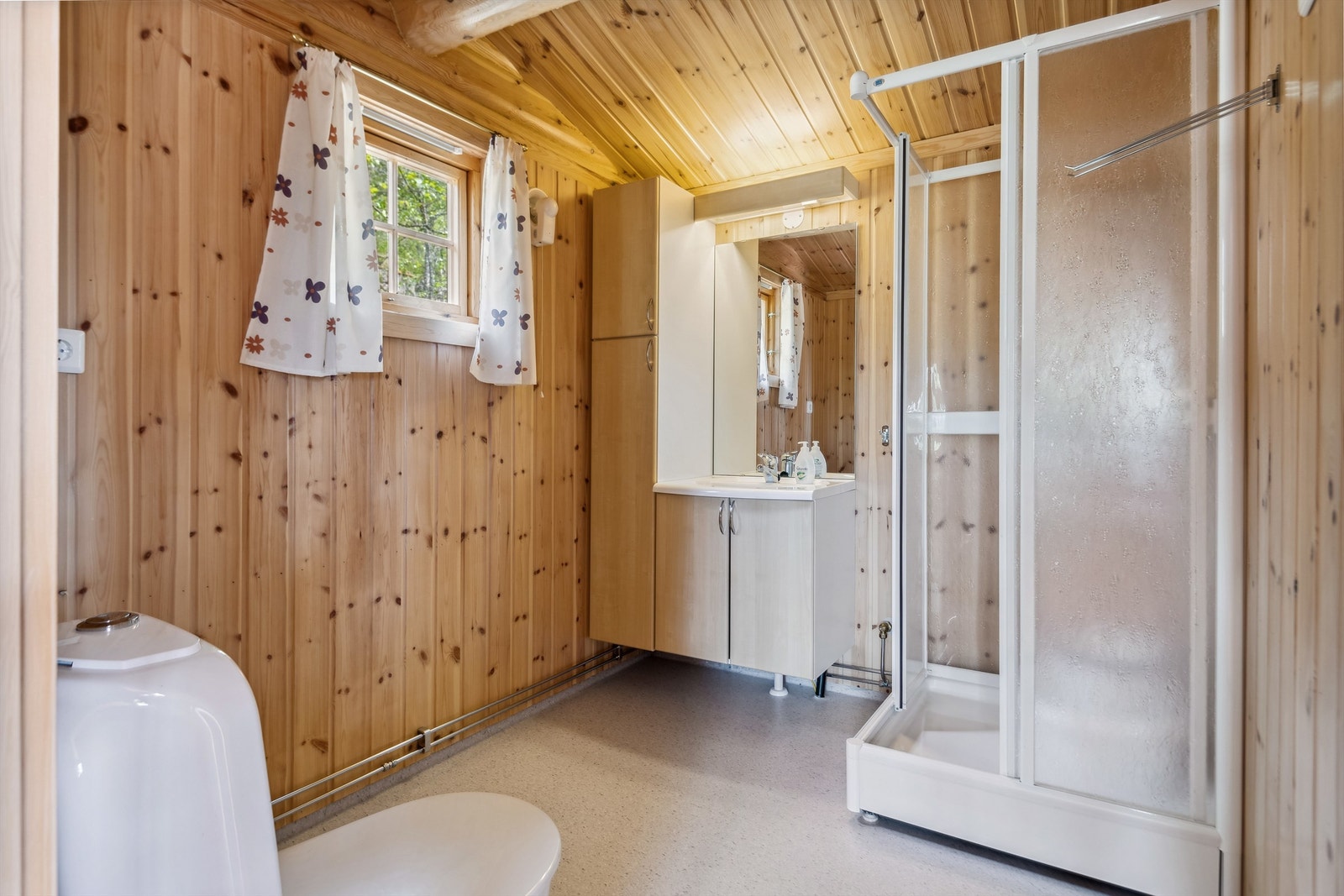 Baderommet har panel på veggene og lyst spraglete belegg på gulvet. Badet er innredet med servant i skapinnredning, høyskap, dusjkabinett og gulvmontert toalett. Veggmontert vifte. Galleribilde