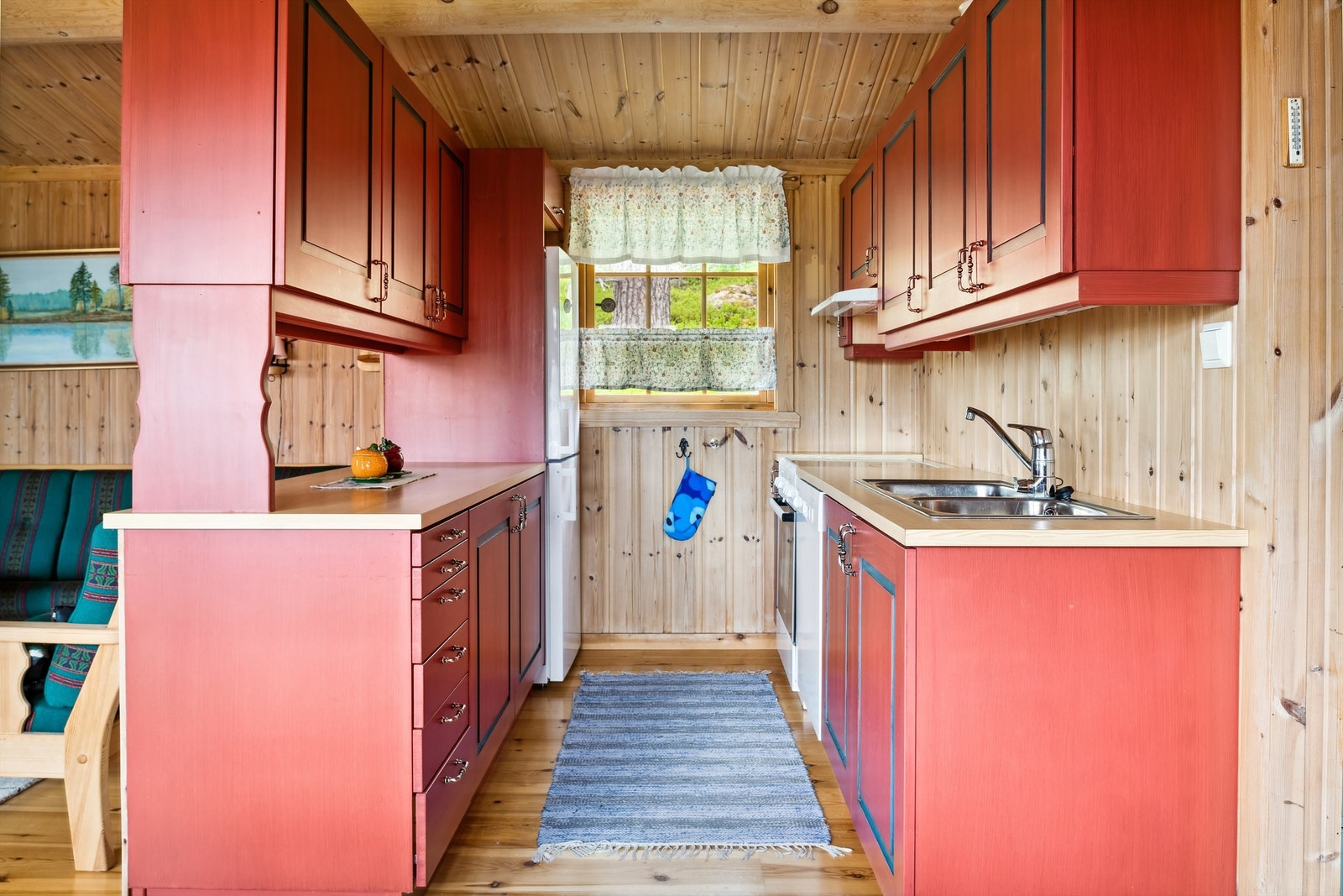 Rød kjøkkeninnredning med profilerte fronter og laminerte benkeplater. Innredningen på to vegger med dels barløsning mot stuen. Innredningen består av overskap, underskap og skuffer. Galleribilde