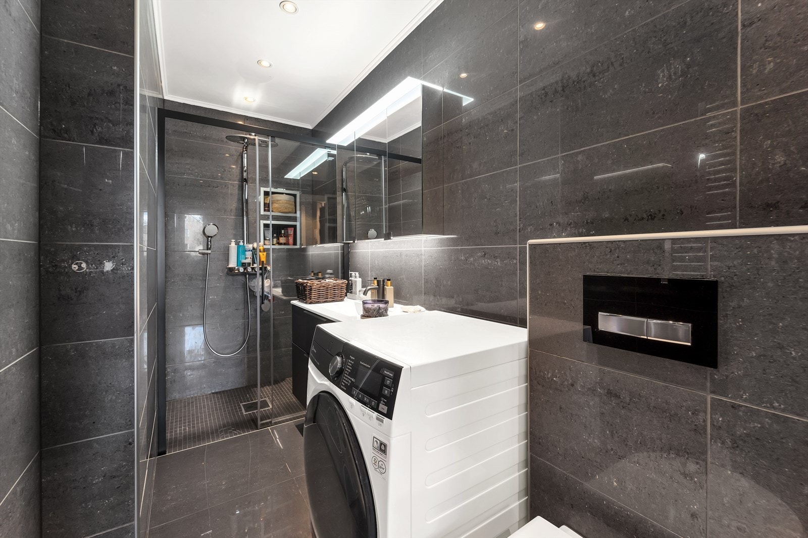 Lekkert, mørkbelagt baderom fra 2014. Overflater er belagt med malte plater og innfelte lys i tak, samt fliser på vegg og gulv. På kaldere høst- og vinterdager bidrar underliggende gulvvarme til ekstra komfor. Galleribilde