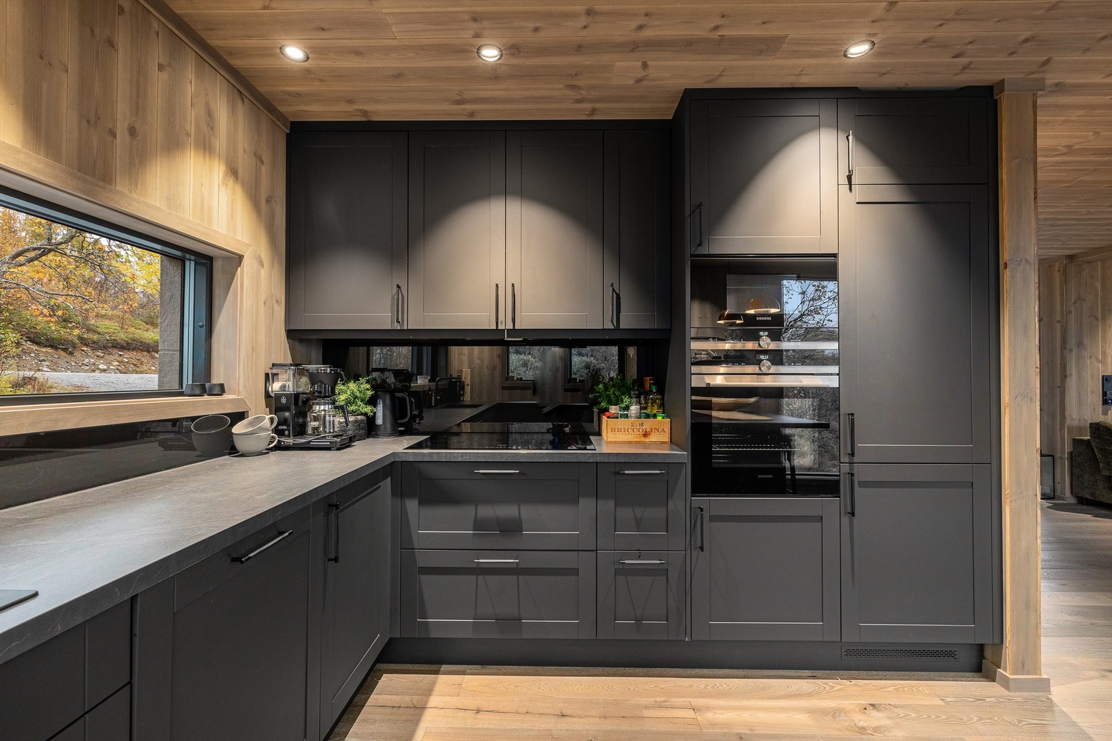 Integrerte hvitevarer som moderne hybridplatetopp med kjøkkenvifte med bevegelsessensor, stekeovn, mikrobølgeovn, kjøleskap med frys og oppvaskmaskin. Galleribilde