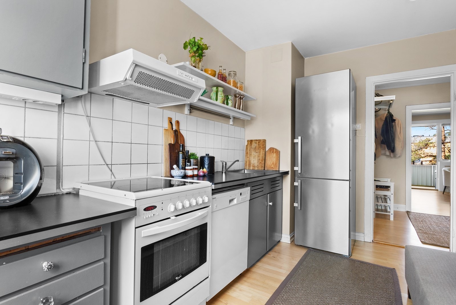 Kjøkkeninnredningen har glatte fronter, fliser på vegg over benkeskap og laminat benkeplate med kum i rustfritt stål. Galleribilde