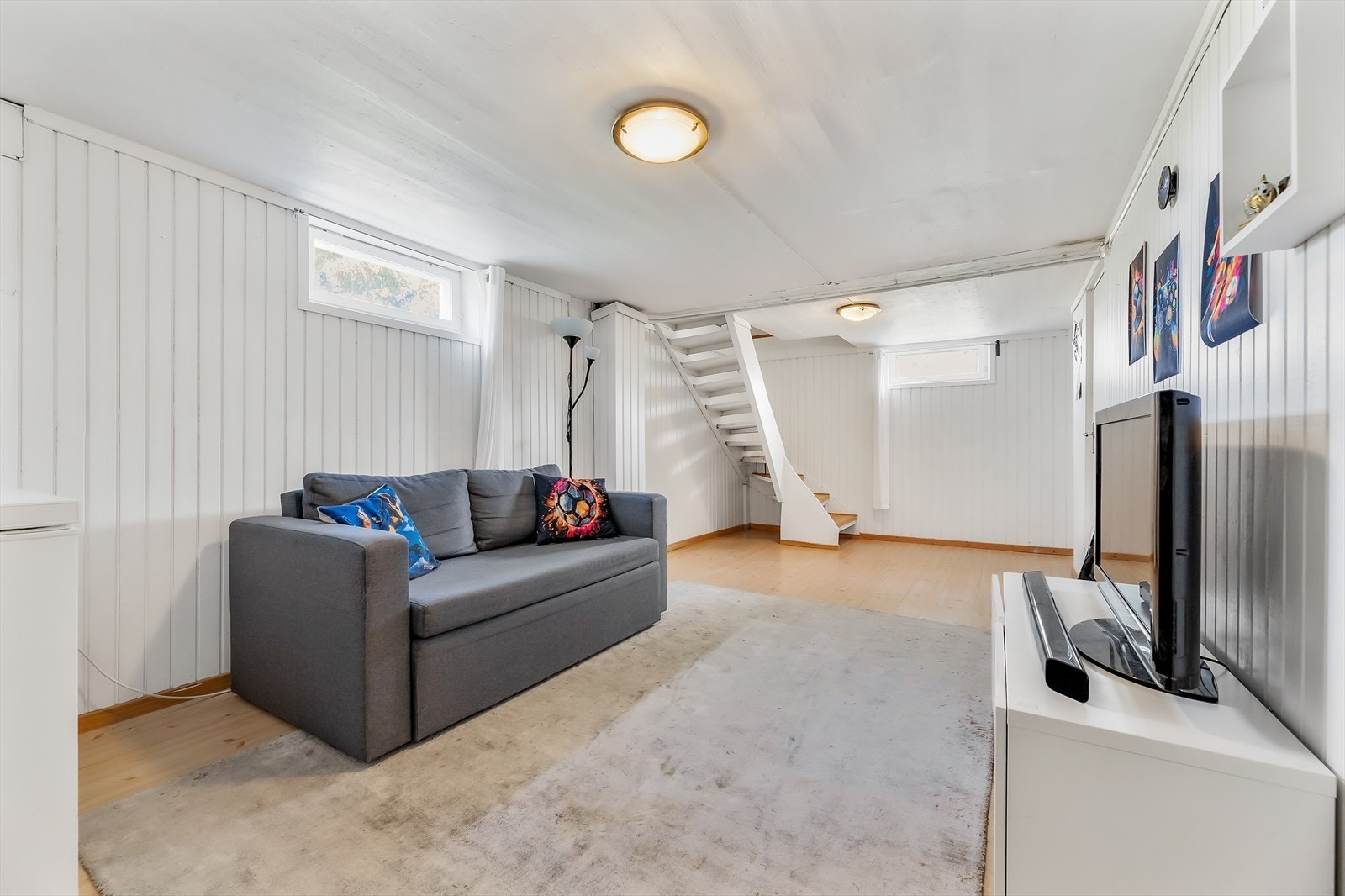 Lyst og romslig kjellerrom med panelerte vegger og laminatgulv Galleribilde