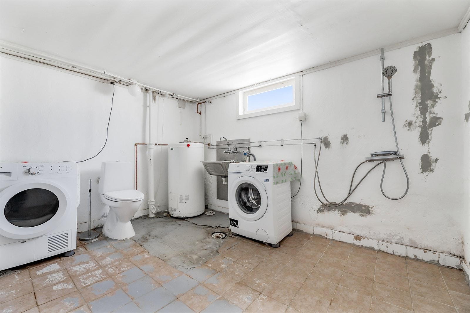 Eget vaskerom av eldre standard, utstyrt med utslagsvask i stål, gulvstående wc og opplegg og plass til både vaskemaskin og tørketrommel Galleribilde