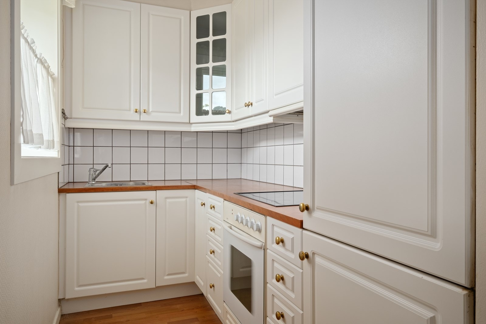 Kjøkken med hvite profilerte fronter, laminat benkeplate, integrert stekeovn, platetopp, kjøl- og fryseskap. Galleribilde