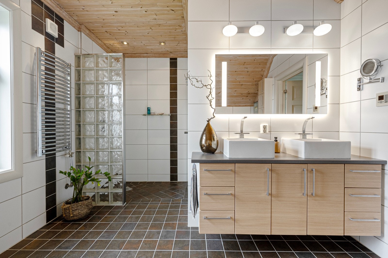 Badet har innredning med glatte fronter og to påstående servanter. Speil med belysning over. Dusjnisje, innebygget hjørnebadekar og vegghengt toalett. Galleribilde