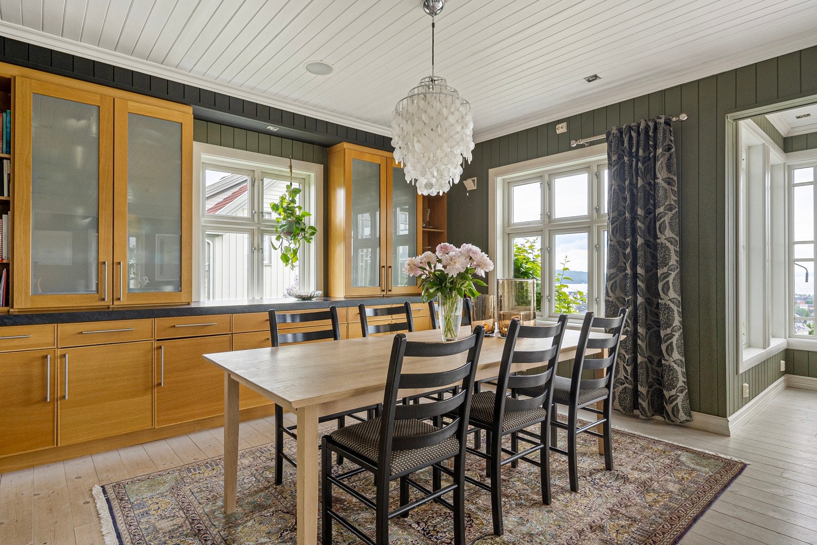 Kjøkkenet er delvis åpent mot spisestuen, og innredningen fra kjøkkenet fortsetter på en smart måte inn i stuen som en skjenk med vitrineskap Galleribilde