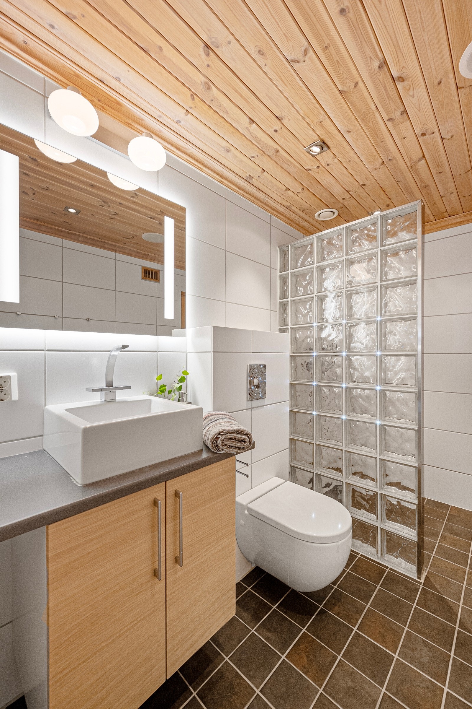 Badet er utstyt med innredning med glatte fronter og påstående servant. Speil med belysning over. Dusjhjørne og vegghengt toalett Galleribilde