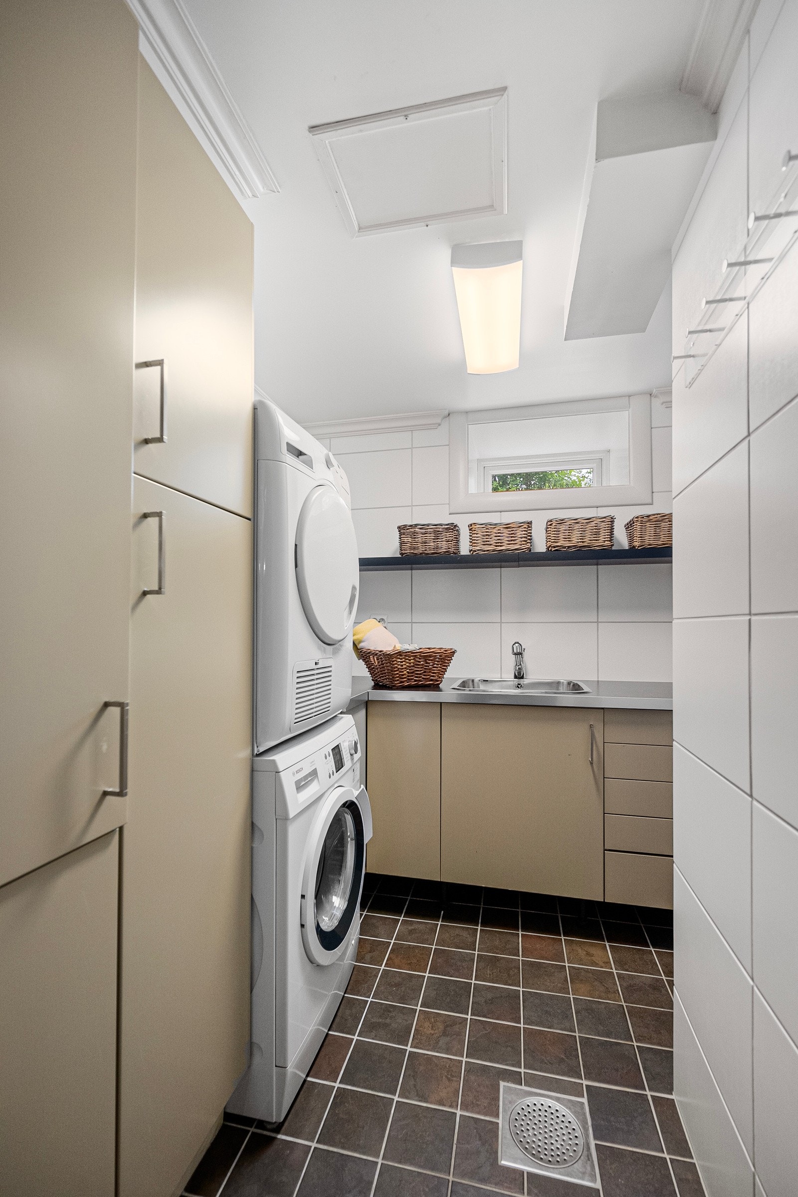 Praktisk vaskerom med fliser på gulv og vegger. Her er innredning med glatte flater og vaskekum samt plass for vaskemaskin Galleribilde