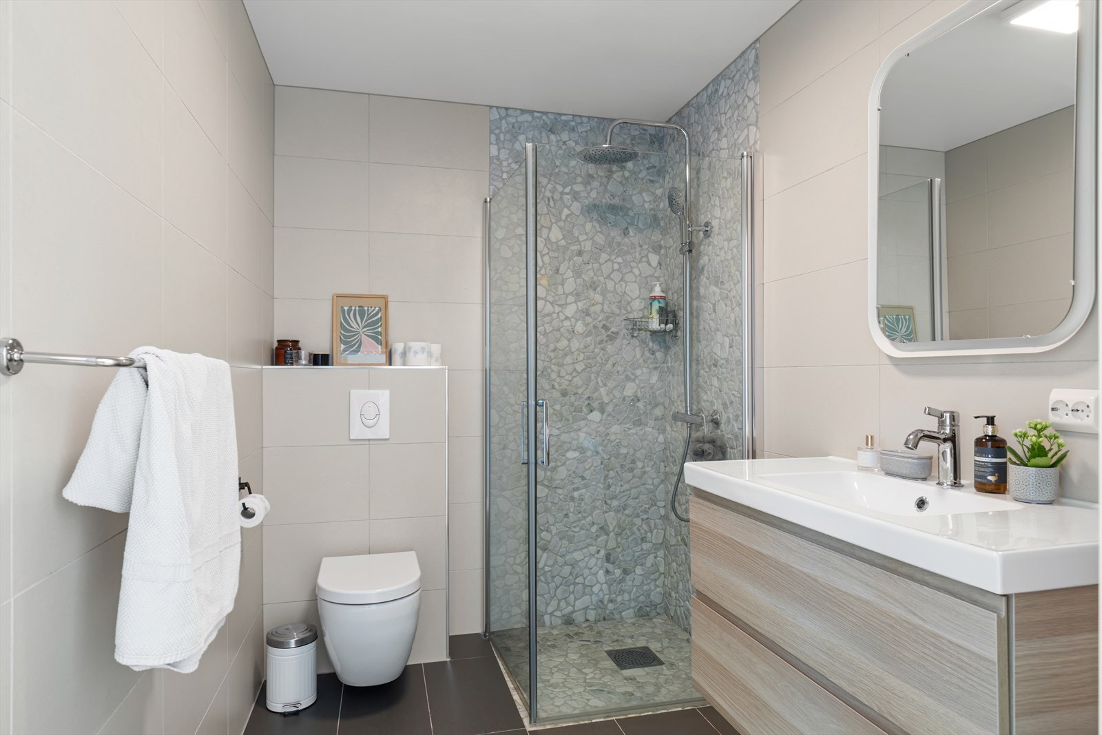 Lekkert helfliset bad med vannbåren gulvvarme, innredet med servant i baderomsmøbel, veggmontert toalett og dusjhjørne. Galleribilde