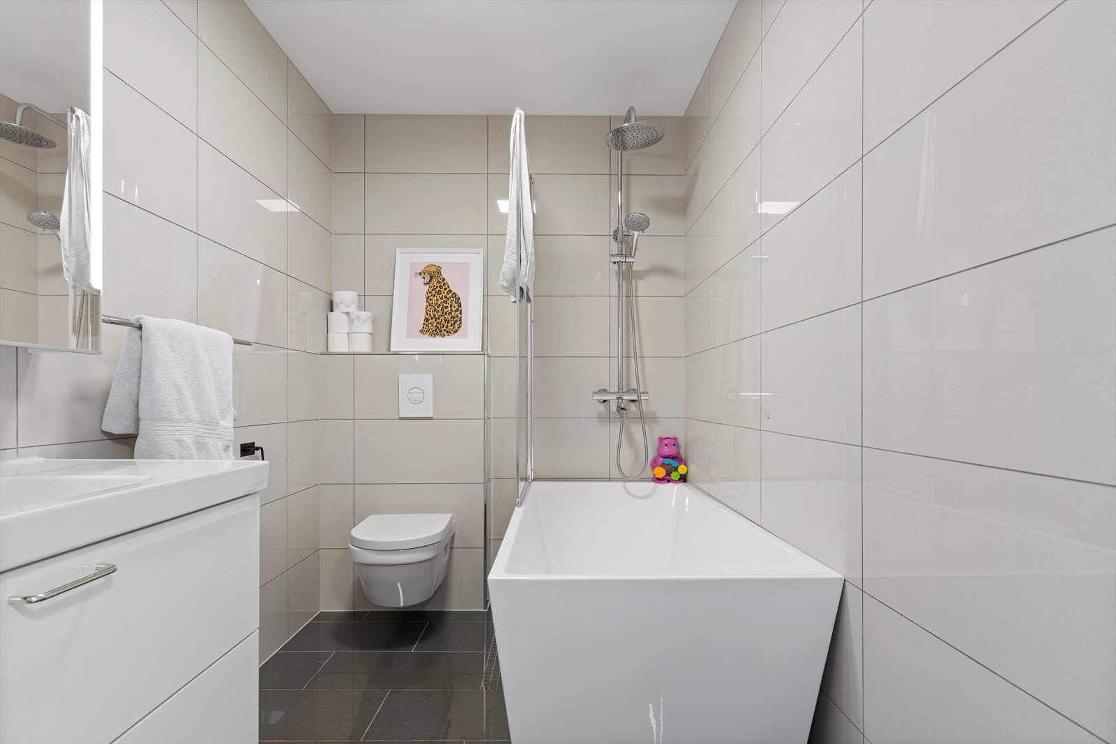 Helfliset bad med vannbåren gulvvarme. Badet er innredet med vegghengt toalett, servant i baderomsmøbel og badekar. Galleribilde