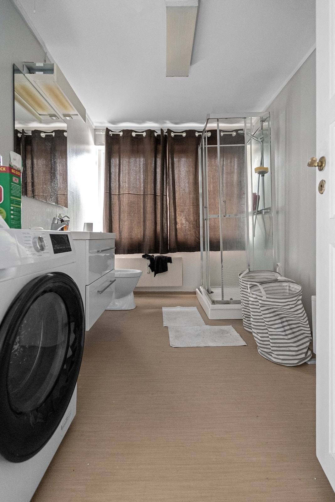 Baderommet har belegg på gulv og lys tapet på veggene. Rommet er utstyrt med moderne baderomsinnredning, dusjkabinett, gulvstående toalett og opplegg for vaskemaskin. Galleribilde