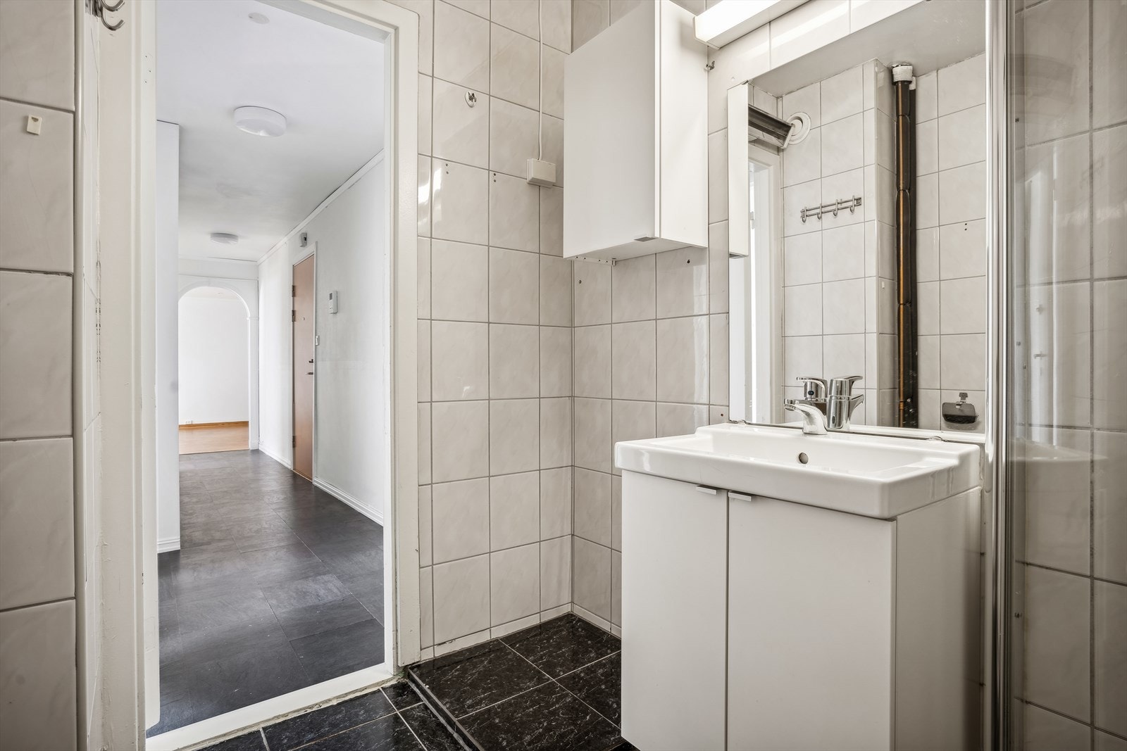 Badet har flislagte vegger, gulv og malte himlinger. Det er servant med baderomsinnredning, dusjhjørne, WC og opplegg for vaskemaskin. Galleribilde