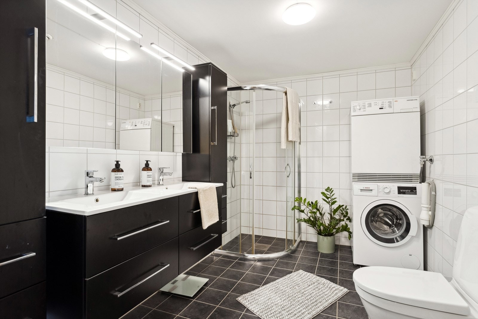 Baderommet inneholder dusjhjørne, gulvmontert wc, servant m/servantskap, speilskap og opplegg for vaskemaskin. Galleribilde