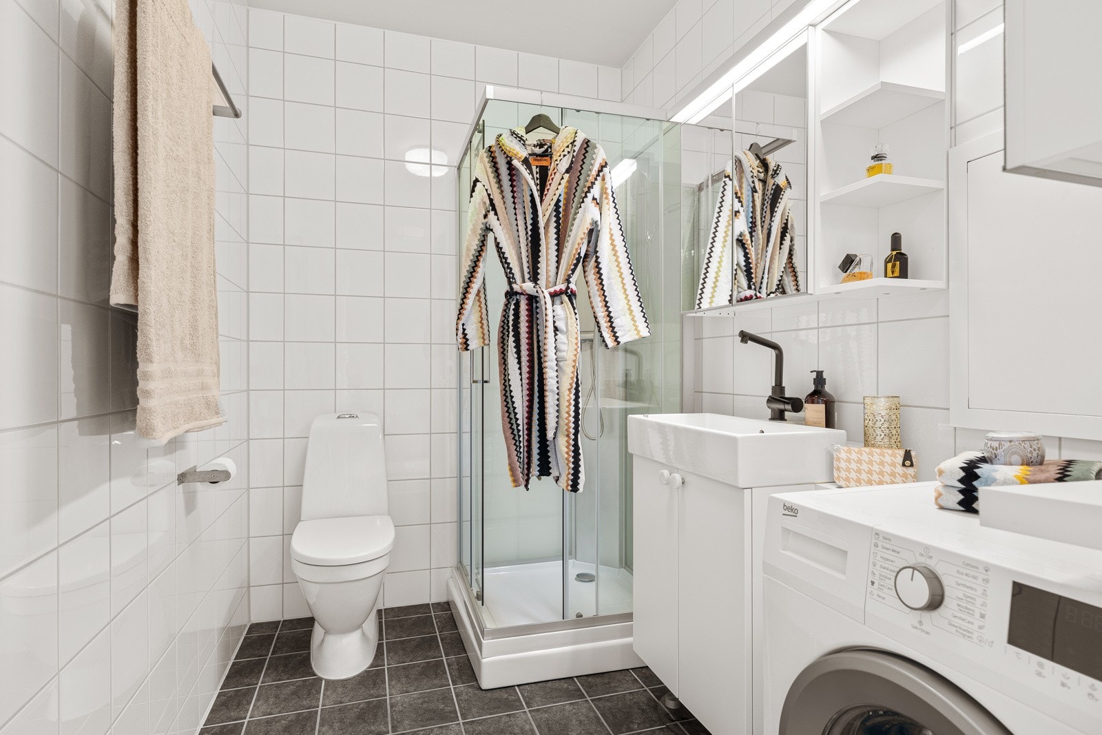 Baderommet er praktisk og målt til ca. 4,5 kvm. Badet har mørkt flislagt gulv med hvite fliser på vegger. Galleribilde