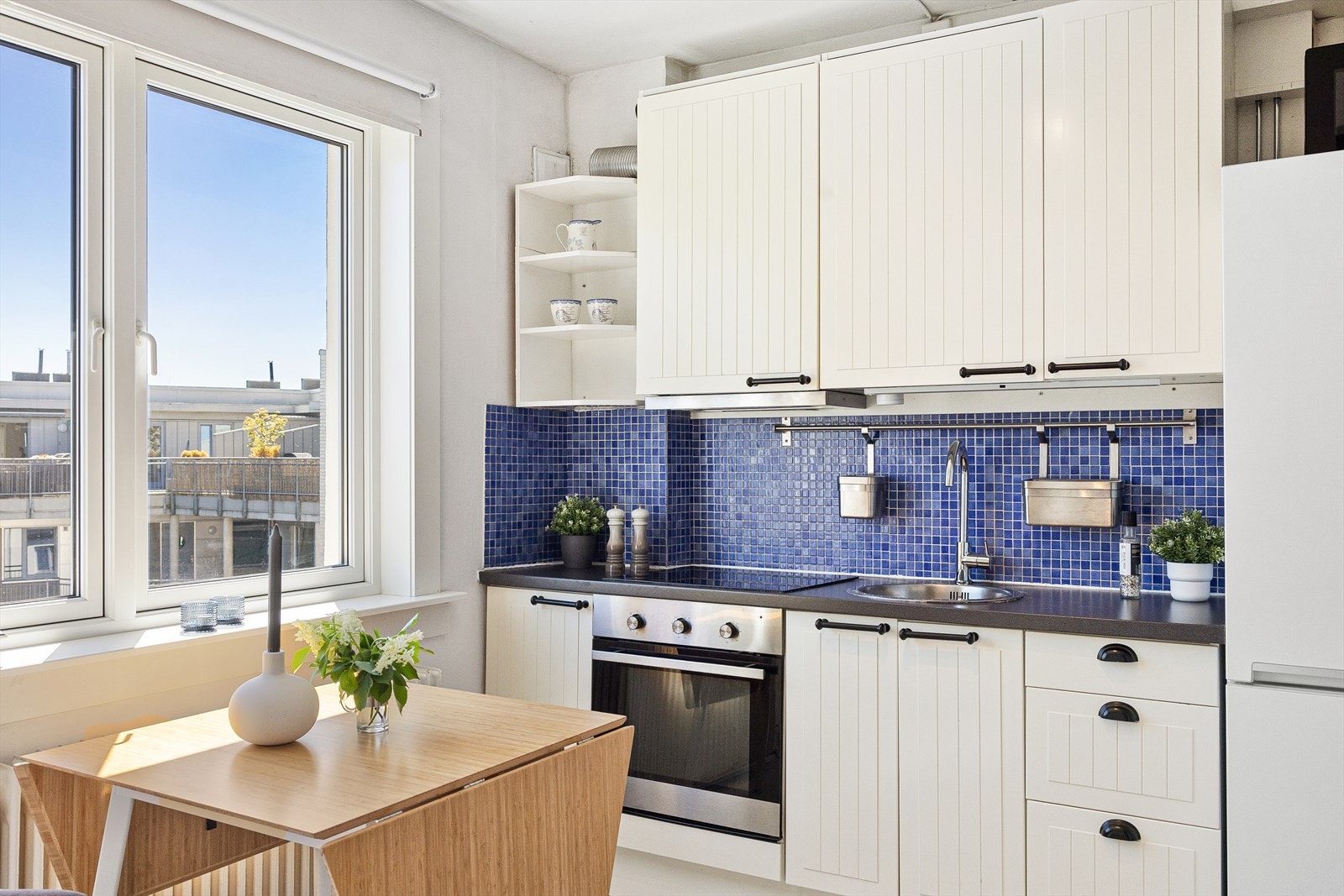 Moderne og stilren IKEA kjøkkeninnredning, fliser mellom overskap og laminert benkeplate, lys under overskap, kum med ettgreps blandebatteri, kullfiltervifte over integrert koketopp/ovn. Galleribilde