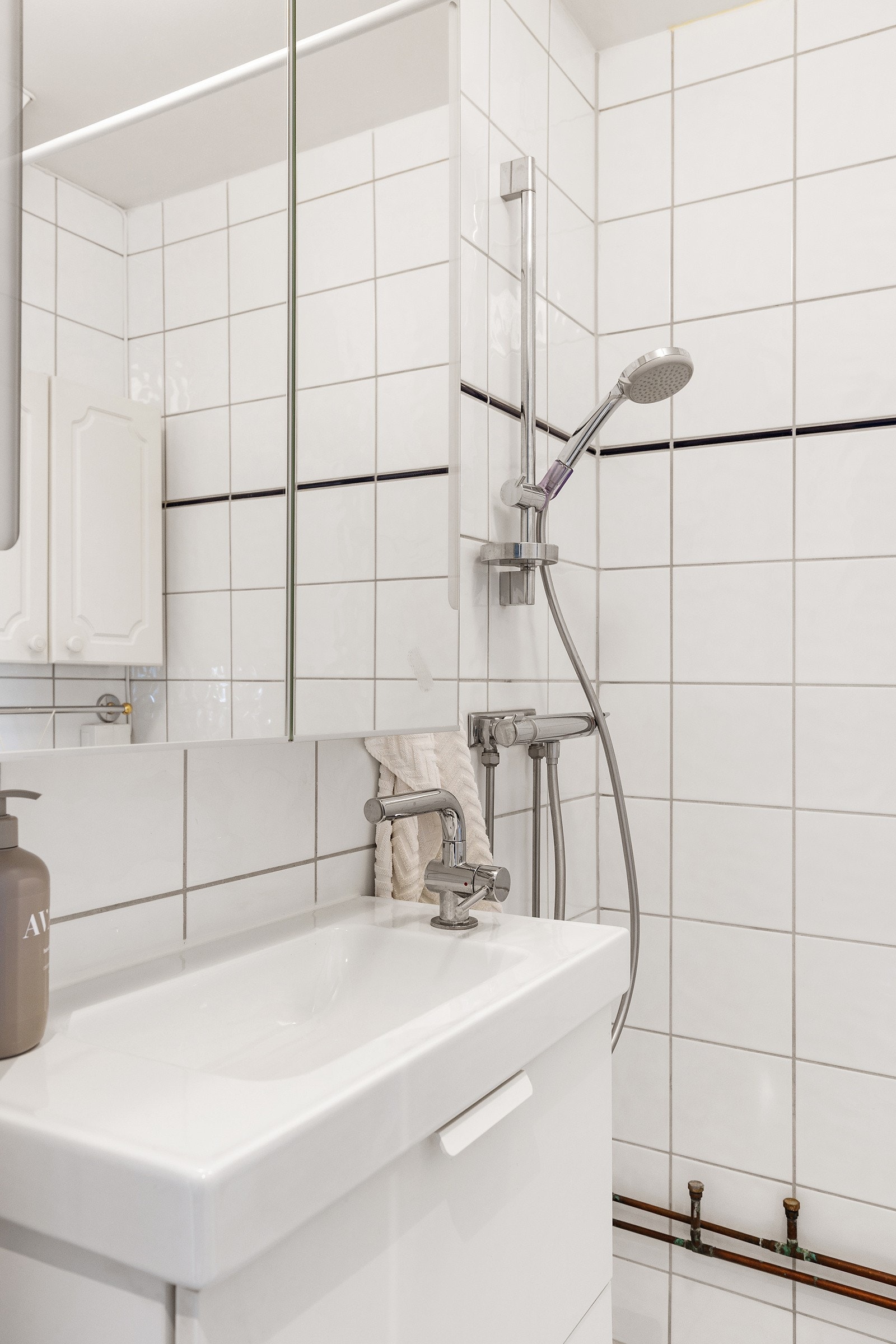 Badet inneholder vegghengt servantskap med skuffer og heldekkende servant, speilskap, wc og dusjhjørne med forheng. Galleribilde