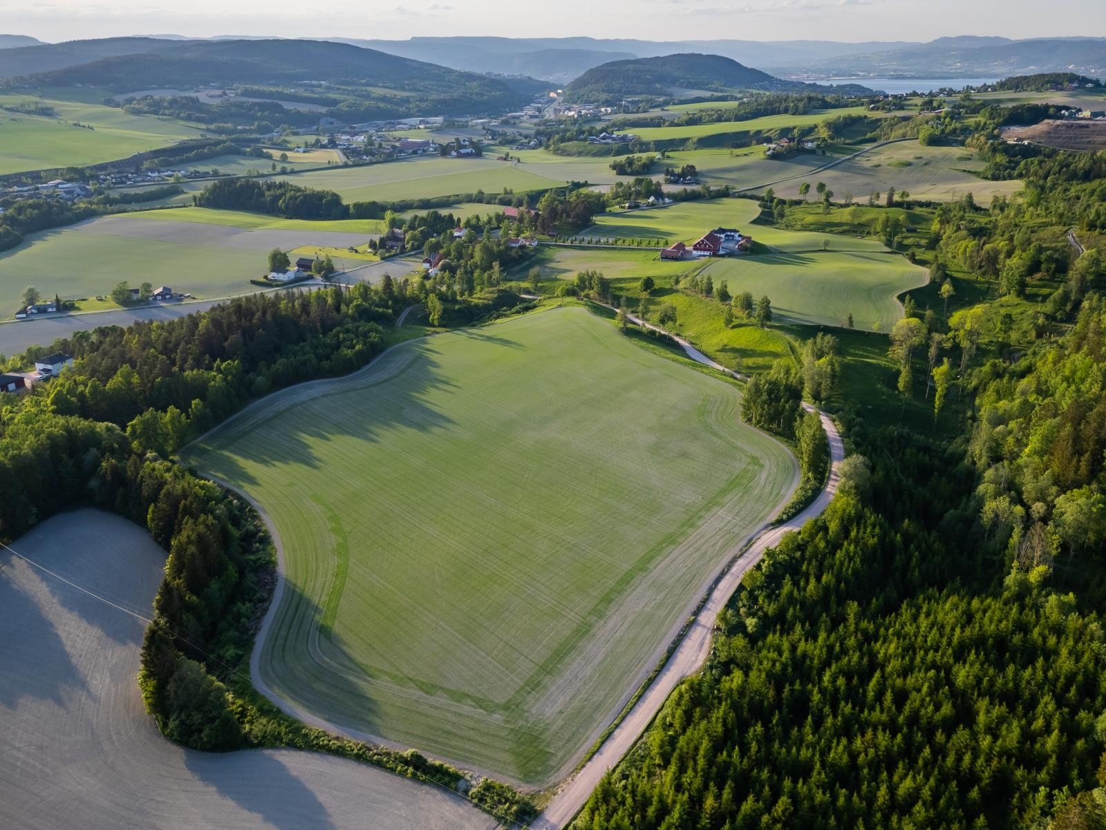 Gården med jordet mot syd i front. På venstre side og høyre side er det noe skog. Galleribilde