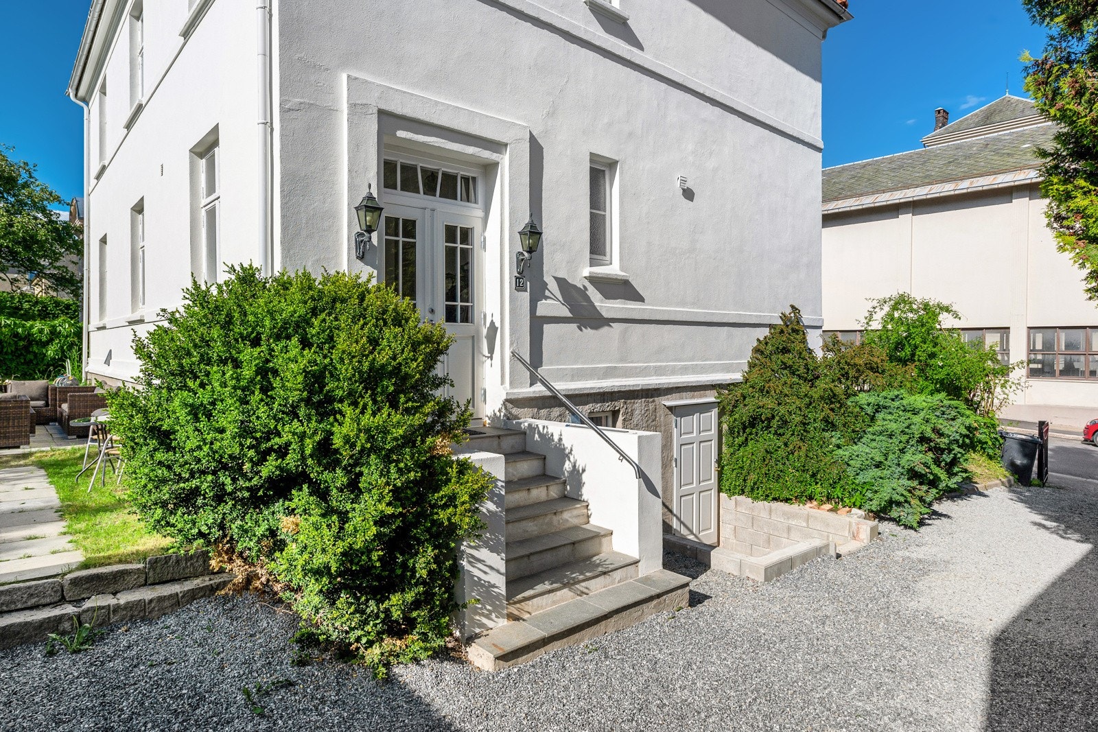 Tomten er hevet fra gateplan med mur og antikt smijernsgjerde, parkering til flere biler og frodig og lun bakhage. Galleribilde