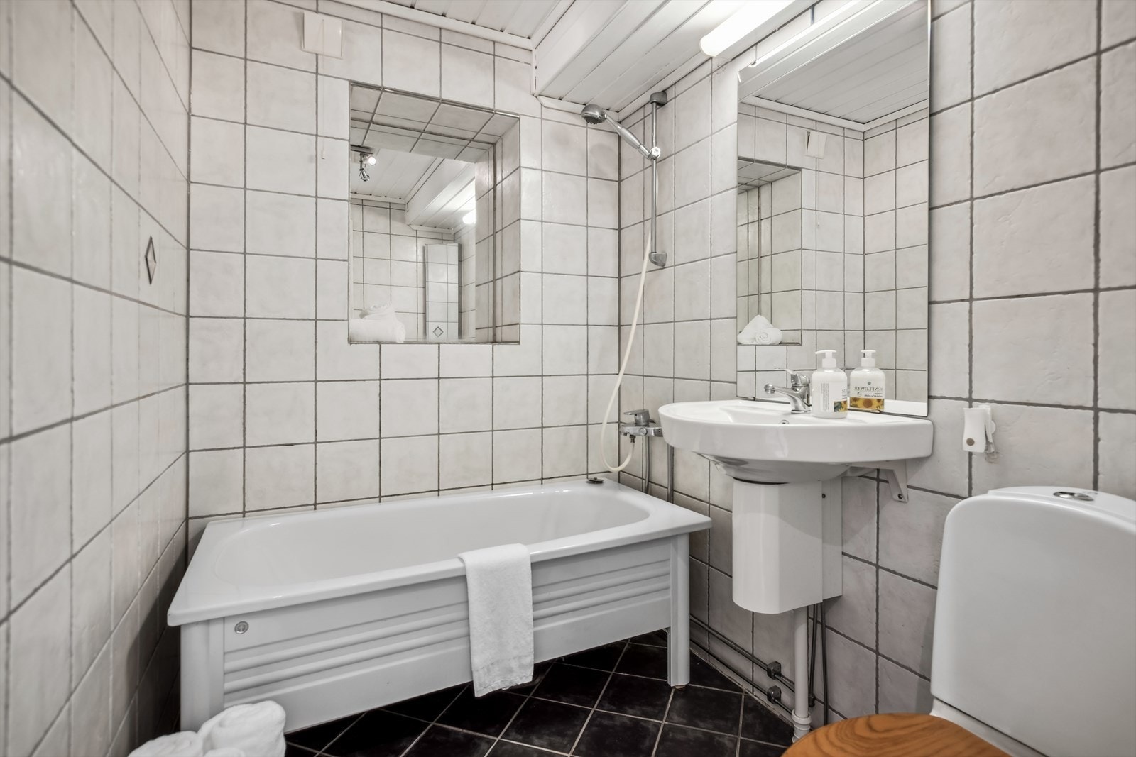 Badet er innredet med toalett, badekar med dusjmulighet, vask i seksjon og speil med belysning. Galleribilde