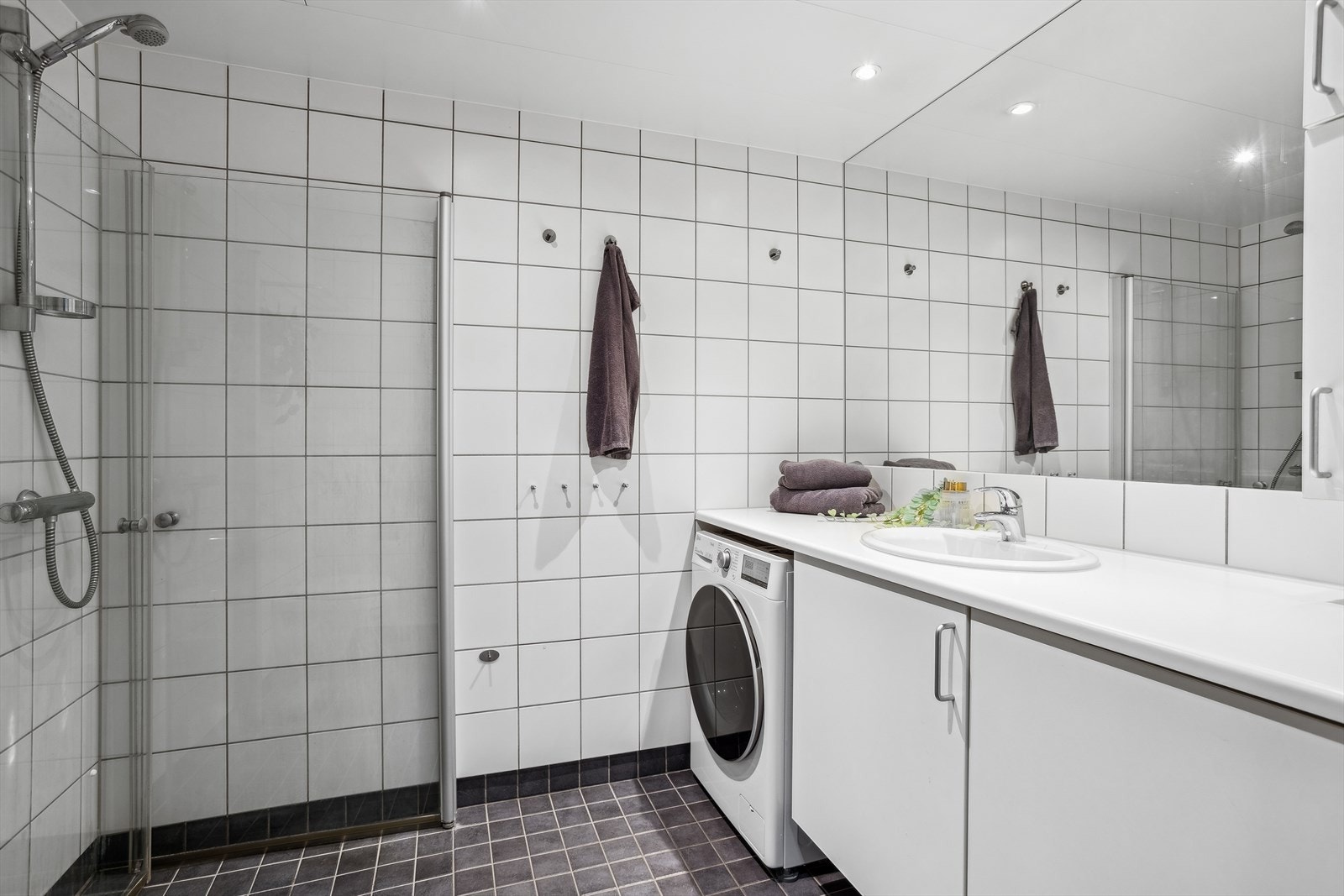 Flislagt bad/wc som består av servant m/underskap, innfliset speil, veggskap, inn-/utadslående dusjdører og opplegg for vaskemaskin. Høyre skapdør kan fjernes til fordel for tørketrommel. Galleribilde