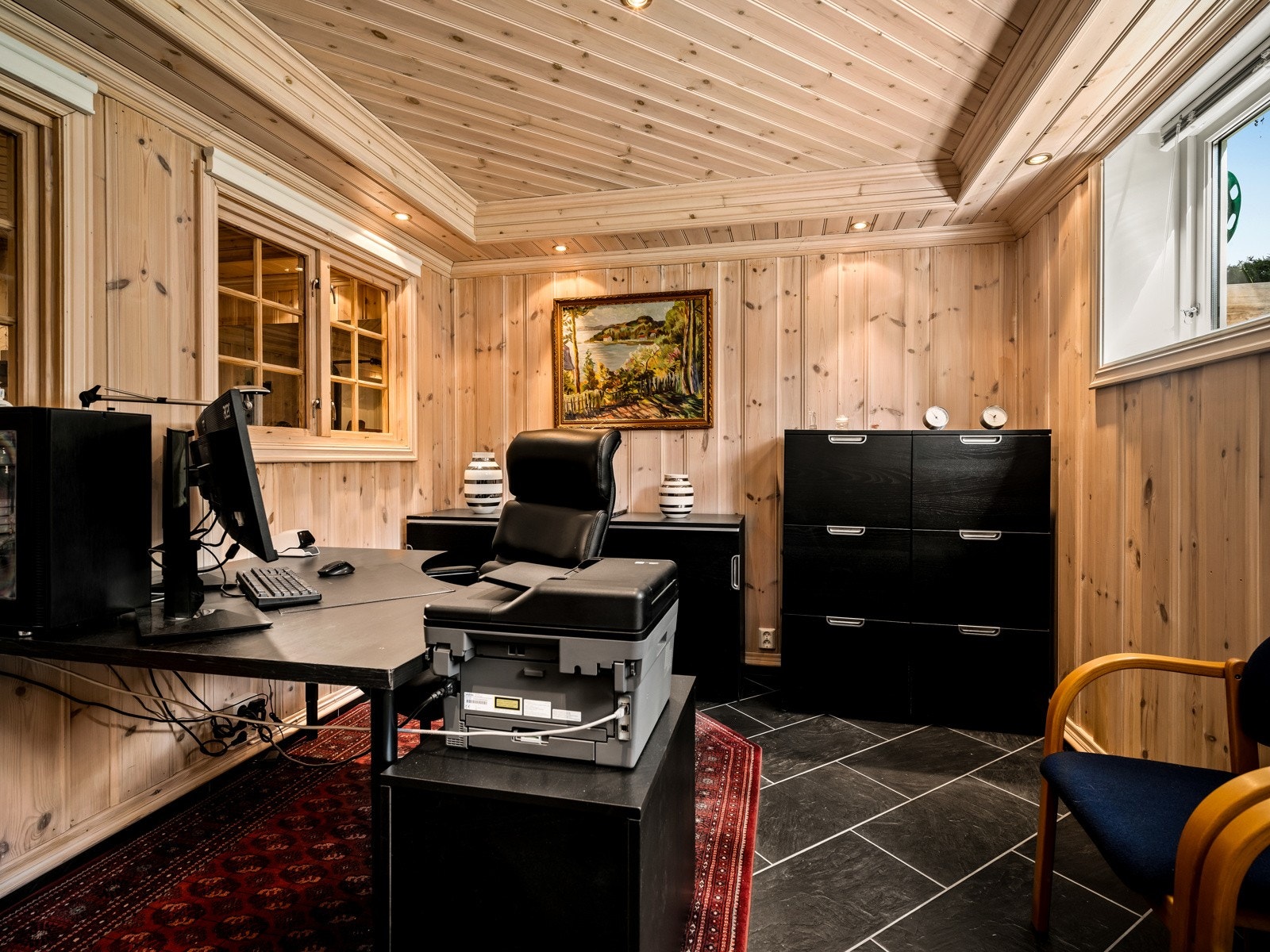 Kontoret har fliser på gulvet, panelvegger og paneltak, samt store vinduer og downligtights i taket. Det er også vinduer fra kontoret inn mot et treningsrom i samme stil. Galleribilde