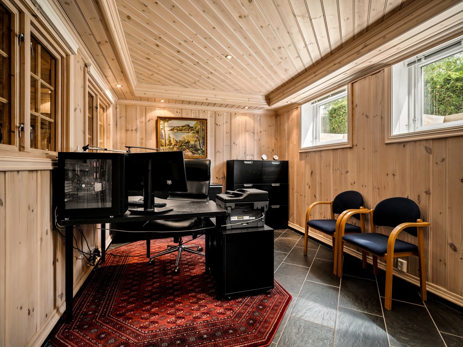 Kontoret har fliser på gulvet, panelvegger og paneltak, samt store vinduer og downligtights i taket. Det er også vinduer fra kontoret inn mot et treningsrom i samme stil. Galleribilde