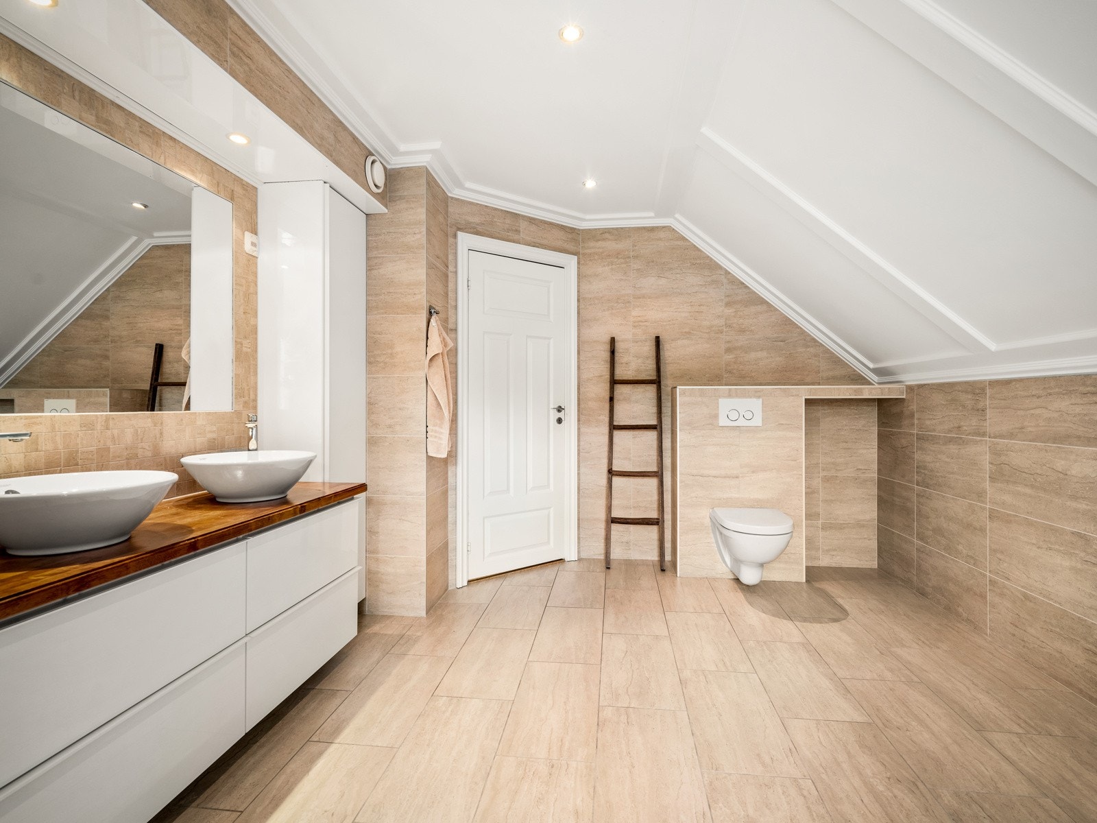 Det er varme i gulvet og downlights i taket/over innredningen. Innredningen består av en benkeplate med to toppmonterte servanter, hvite underskuffer og hvite høyskap. Over servantene er det speil. Galleribilde