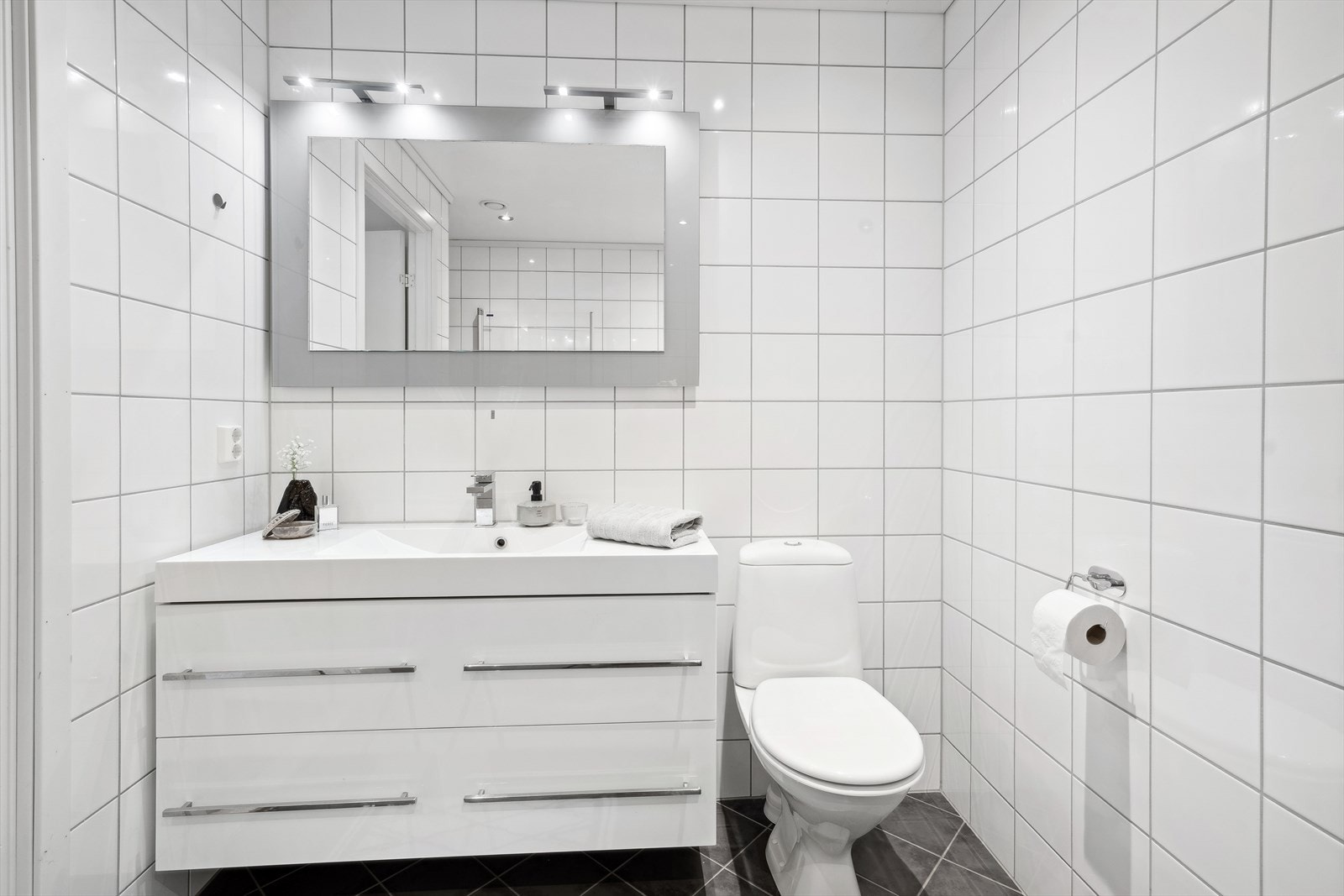 Badet er innredet med speil, servant med skuffeseksjon, toalett og dusjhjørne. Galleribilde