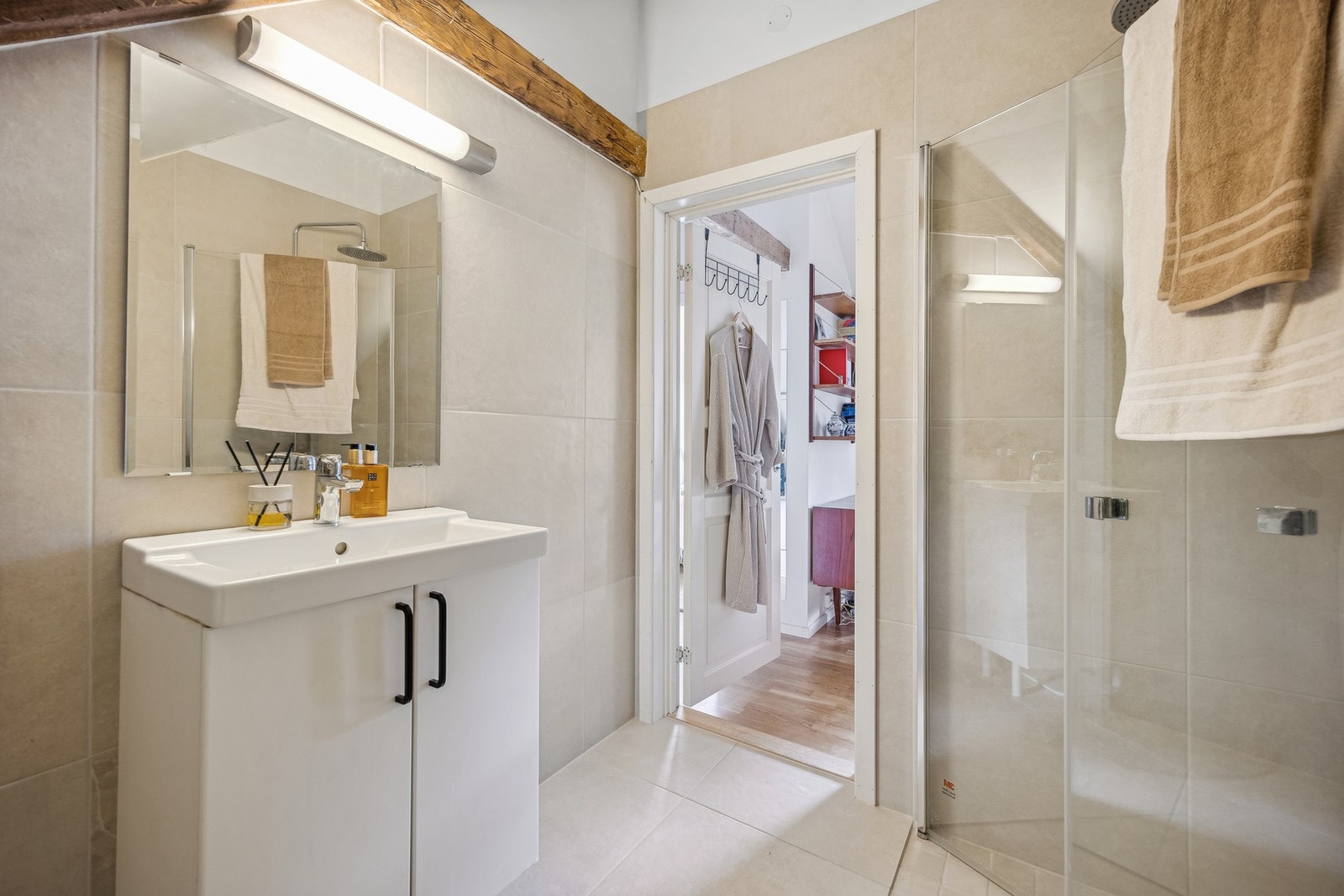 Badet er utstyrt med plassbesparende dusjdører i glass og servantinnredning med lagring. Galleribilde