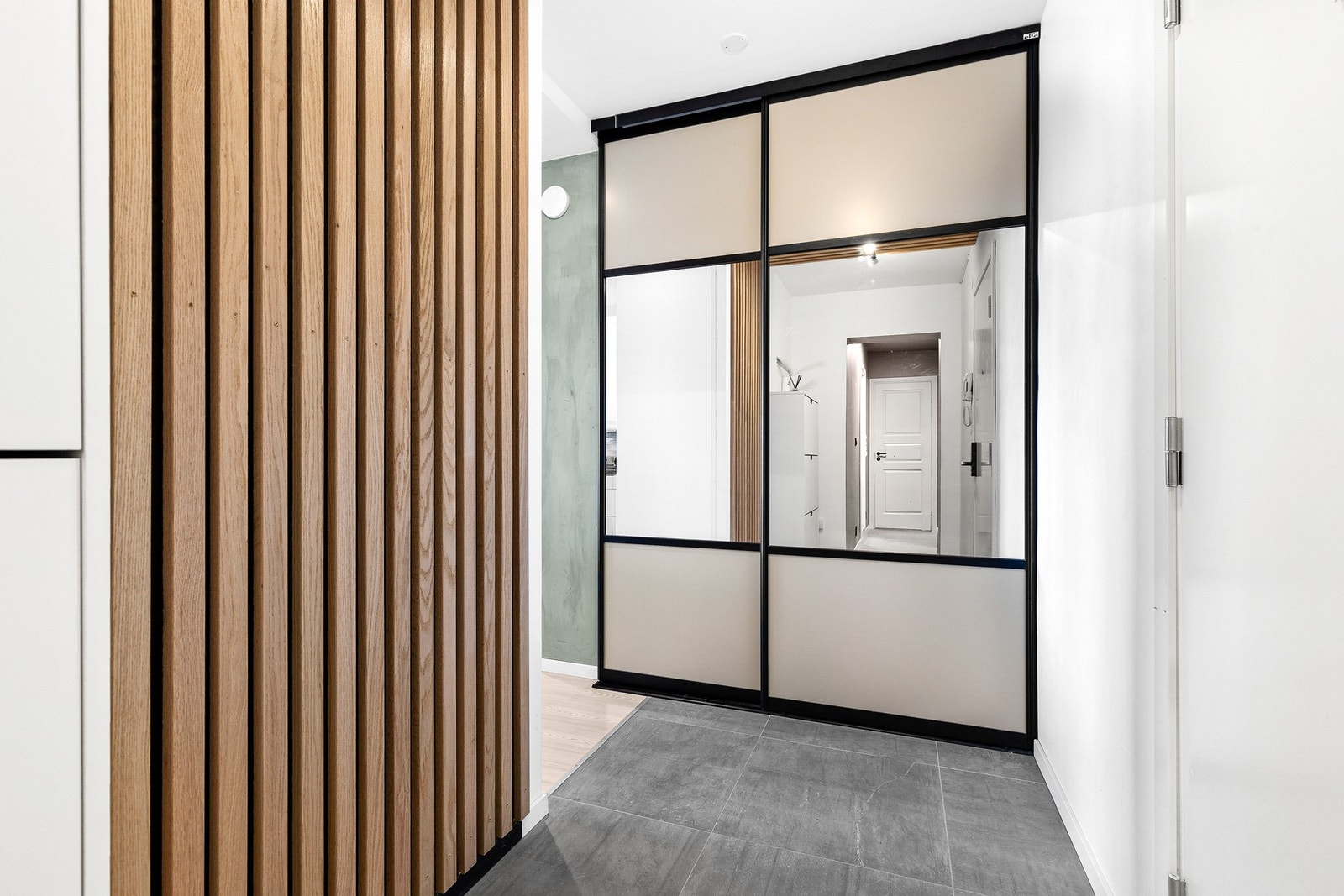 Gang/entre med store fliser på gulv, spilervegg og skyvedørsgarderobe m/speil. Galleribilde