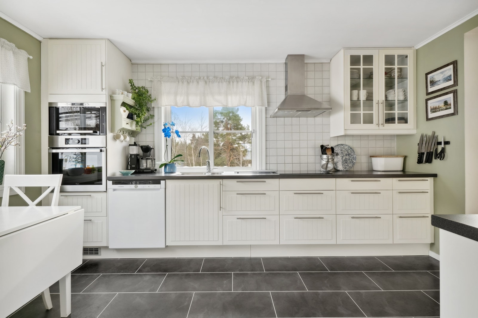 Kjøkkenet har mosegrønne malte plater på veggene og grå flislignende laminat på gulvet. Kjøkkeninnredning med profilerte fronter og laminerte benkeplater. Galleribilde