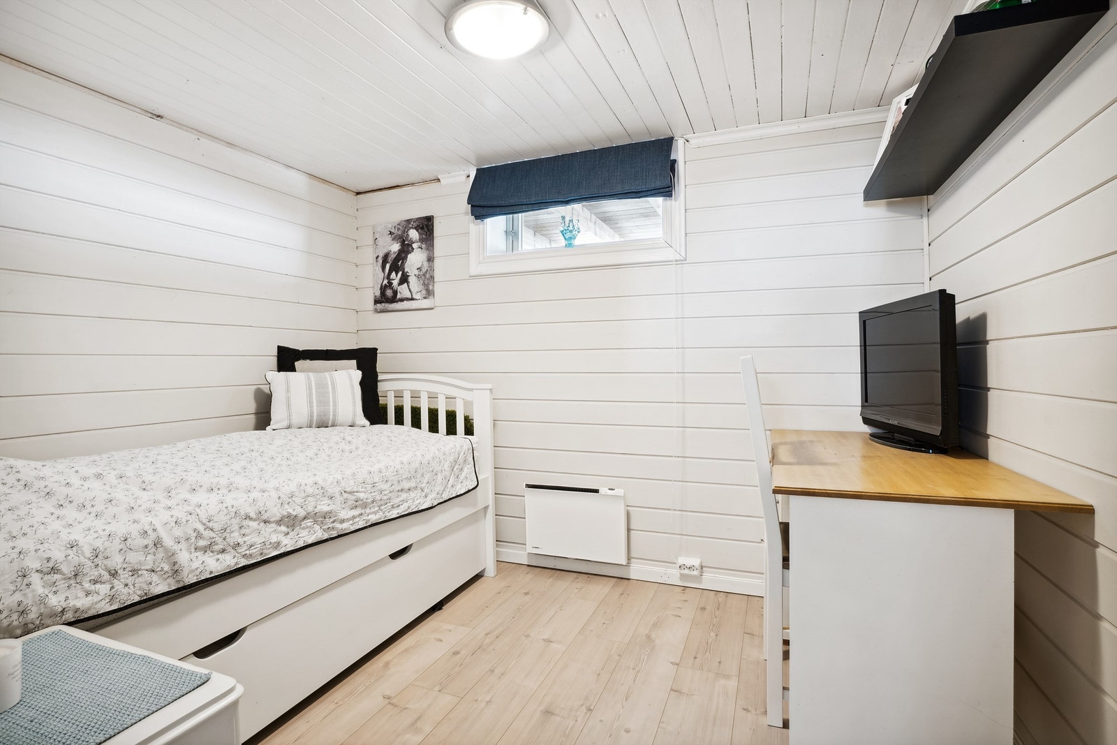 Det andre disponible rommet i kjelleren har også lysmalt panel på veggene og lys laminat på gulvet. Innredet som soverom/gjesterom.
Rommet er ikke godkjent til varig opphold. Panelovn på vegg som varmekilde. Galleribilde