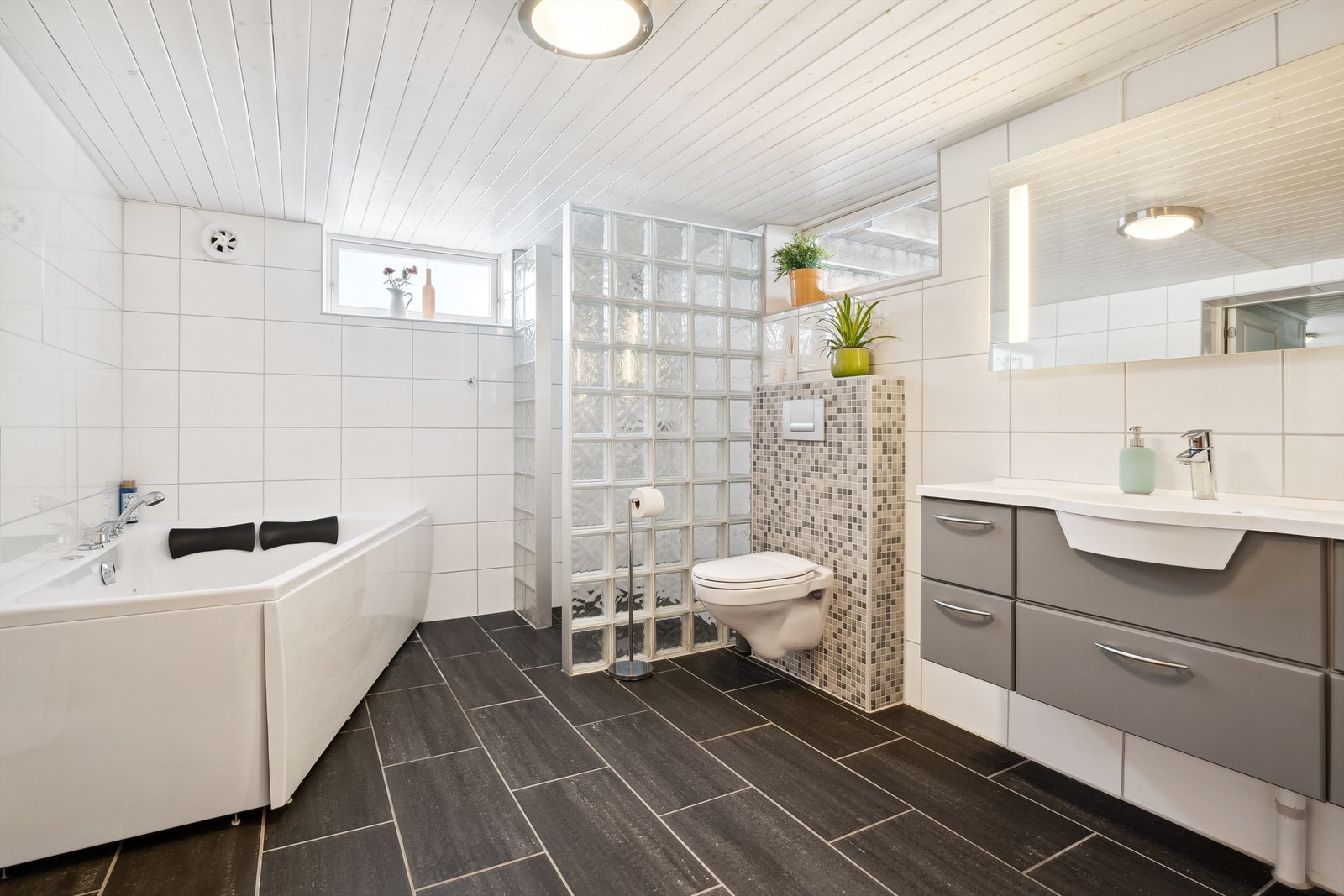 Baderom i kjelleren har hvite fliser på veggene og grå/svarte fliser på gulvet. Galleribilde