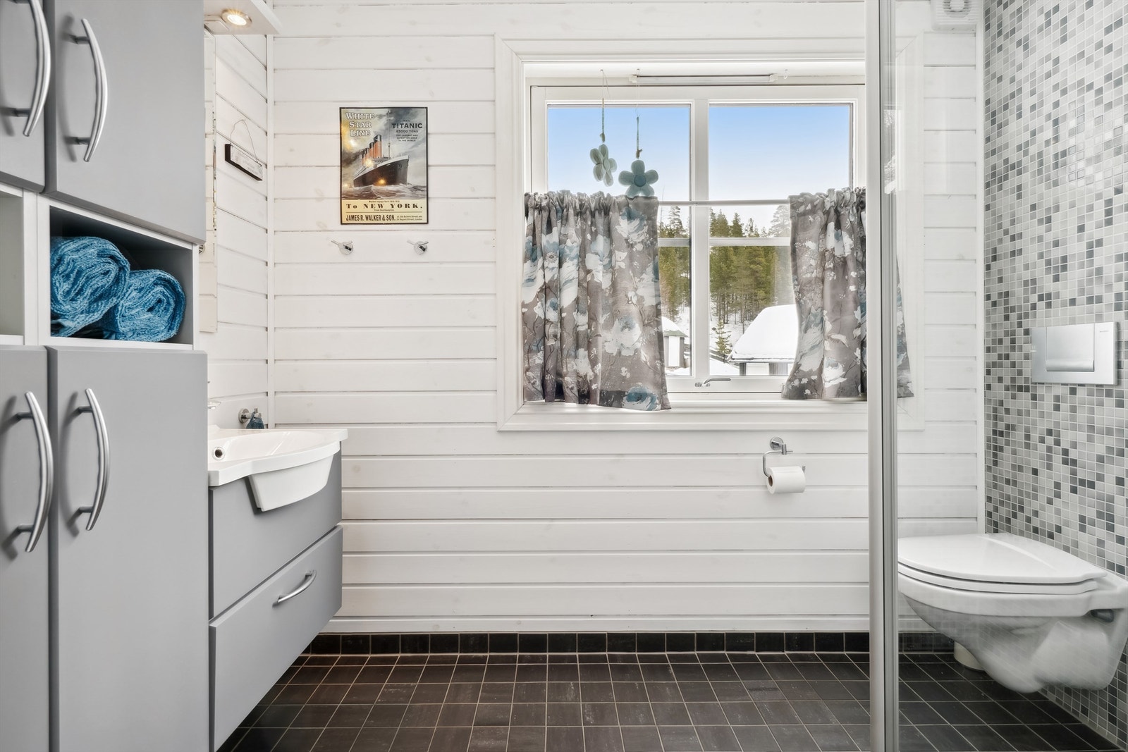 Badet er innredet med servant i grå skuffeinnredning, vegghengte skap, veggmontert toalett og dusjhjørne. Galleribilde