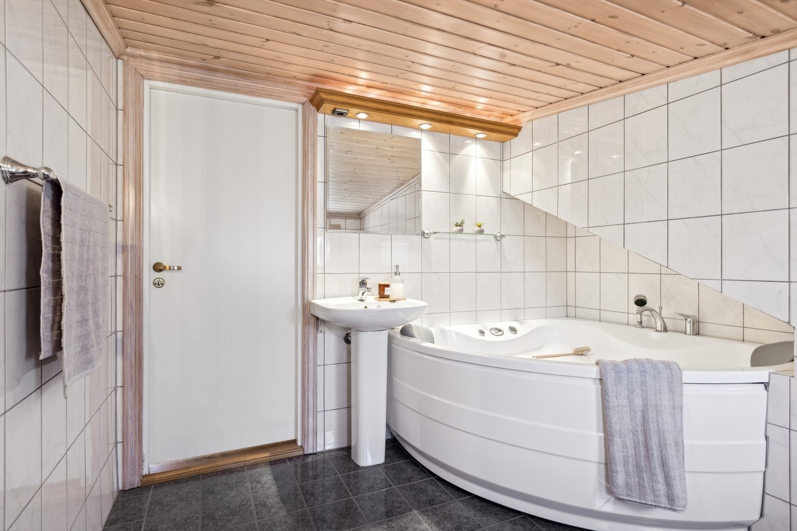 Dette baderommet er også med fliselagte overflater på vegger og gulv. Videre er rommet utstyrt med servant med blandebatteri, badekar med multifunksjon og gulvmontert toalett. Det er varmekabler i gulvet her. Galleribilde