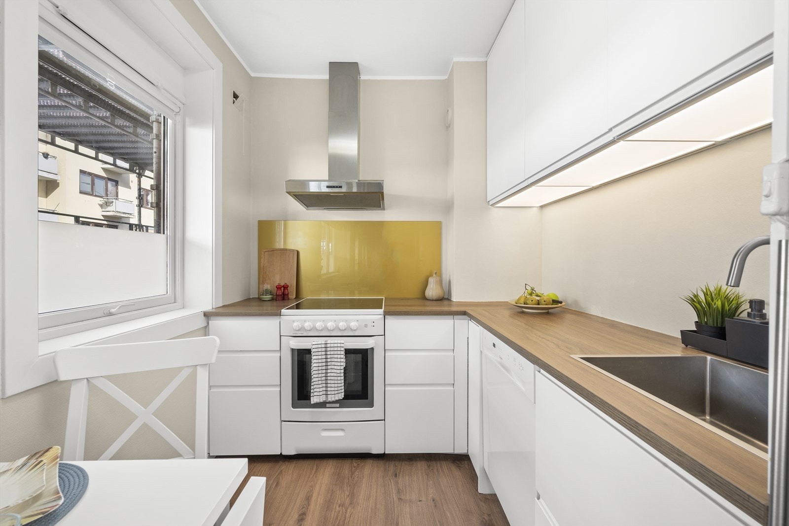 Kjøkkenet har opplegg for oppvaskmaskin, komfyr og kjøleskap og innredningen består av hvite slette høyglansfronter med laminert benkeplate. Galleribilde