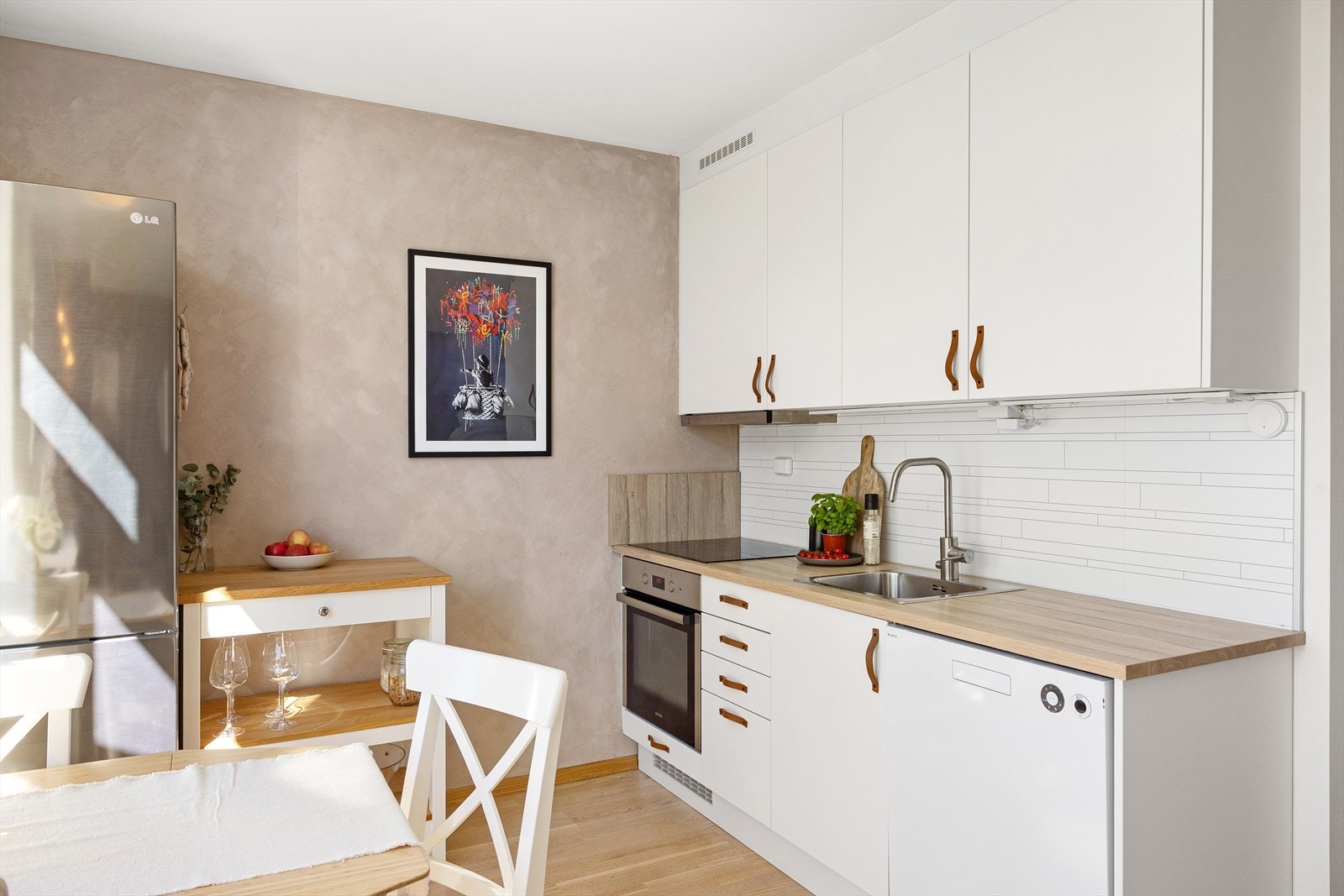 Moderne og stilren kjøkkeninnredning bestående av glatte laminerte fronter, plater mellom overskap og laminert benkeplate, kum med ettgreps blandebatteri, vifte over integrert koketopp/ovn, lys under overskap og opplegg for oppvaskmaskin. Galleribilde