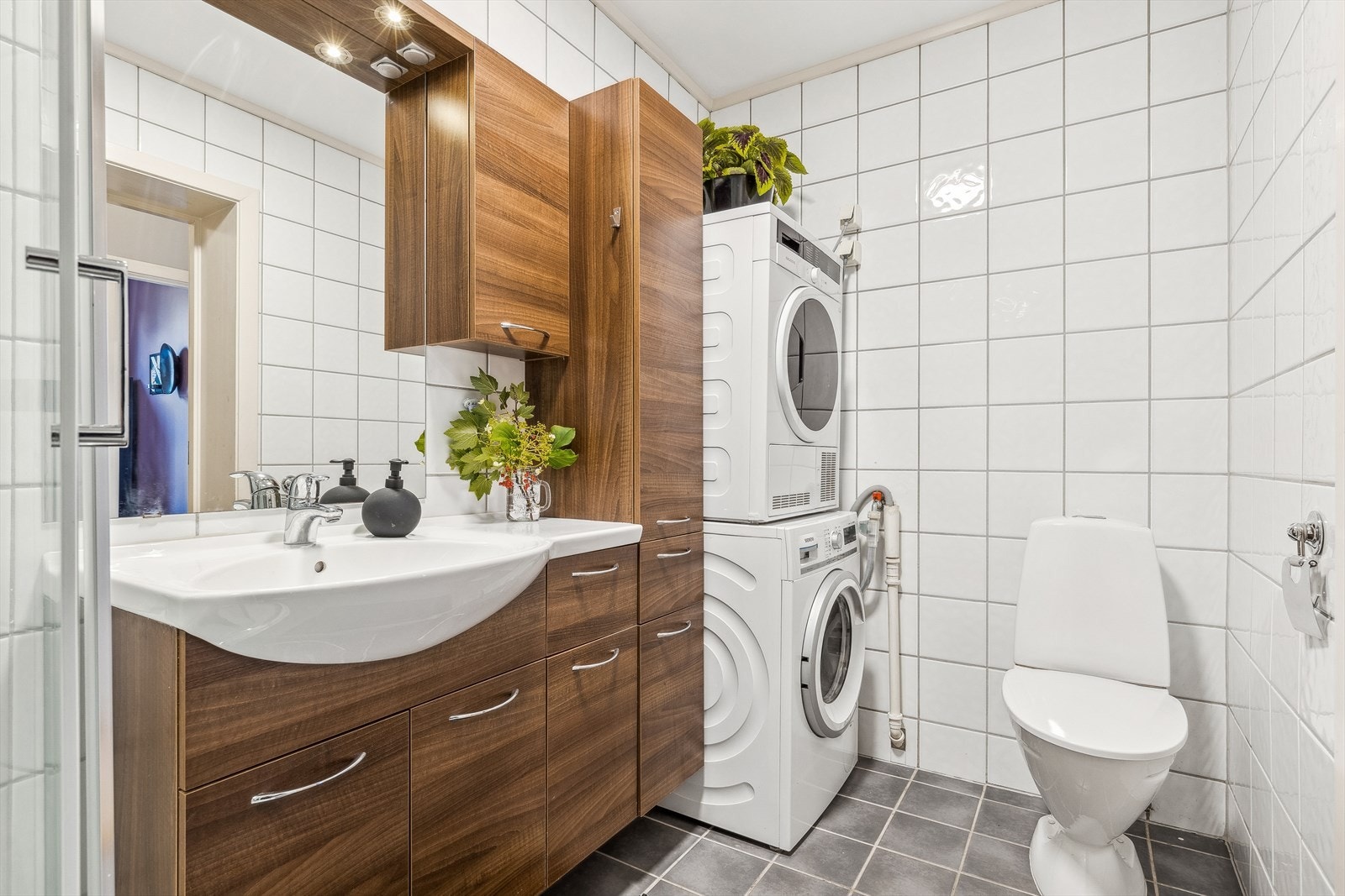 Videre er rommet utstyrt med servantinnredning, speil, dusjkabinett og toalett. Det er opplegg for vaskemaskin og plass til tørketrommel på badet her. Galleribilde