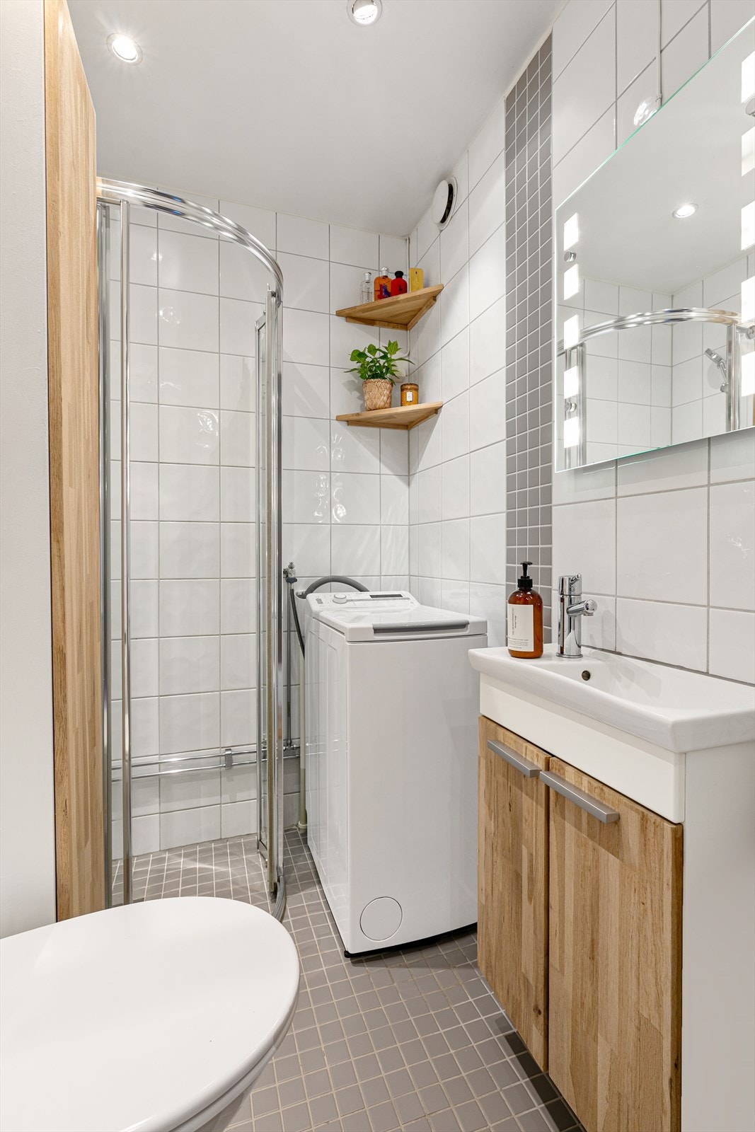 Baderommet er pent flislagt og inneholder alt dere trenger med baderomsinnredning med heltre fronter og heldekkende servant, speil med lysarmatur, dusjhjørne med buede skyvedører og veggmontert toalett. Det er også opplegg for vaskemaskin (smal modell). Galleribilde